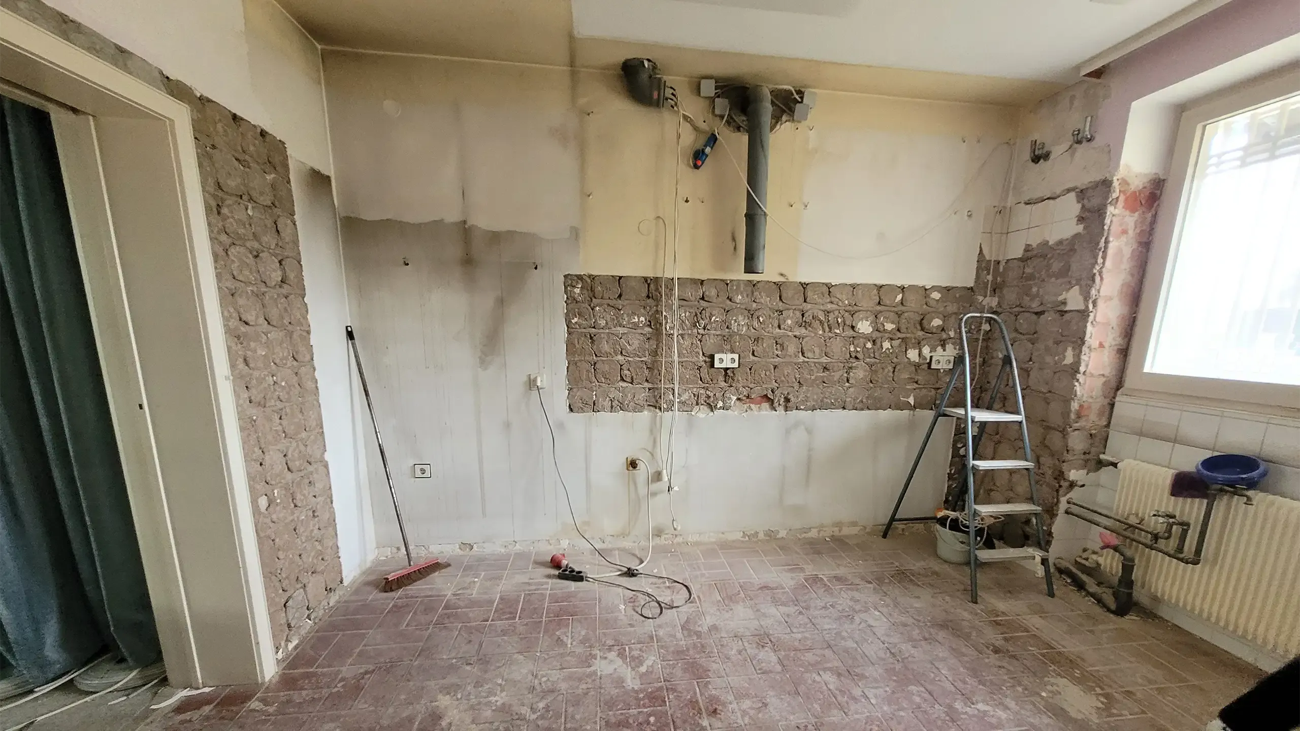 Vorher-Aufnahme: Altbau-Küche im Sanierungszustand mit abgeschlagenen Wandfliesen und altem Heizkörper.