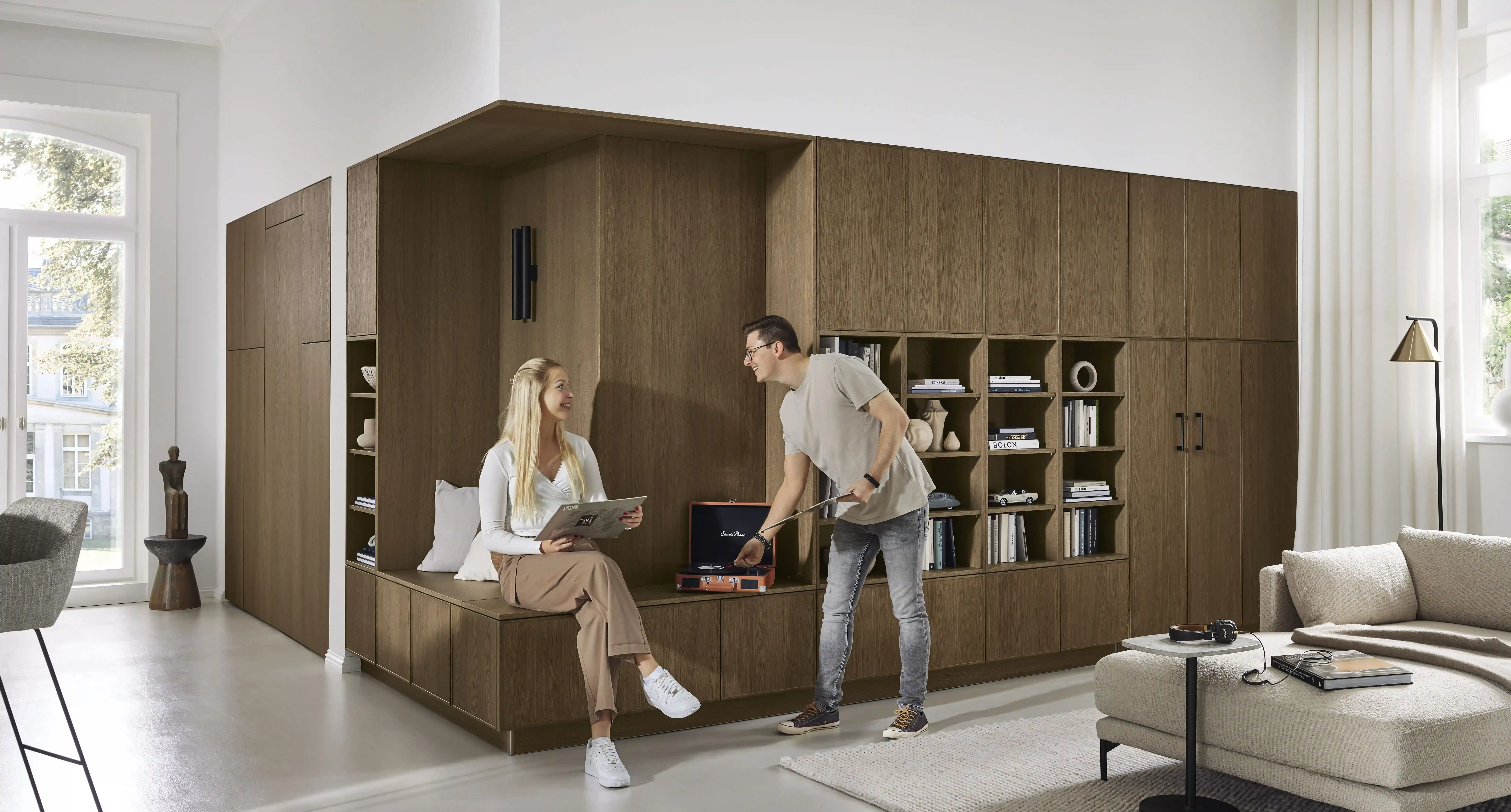 Paar an wohnlicher Bibliothekswand in Nussbaum mit Sitzbank, Sideboard und Schrankbett-System