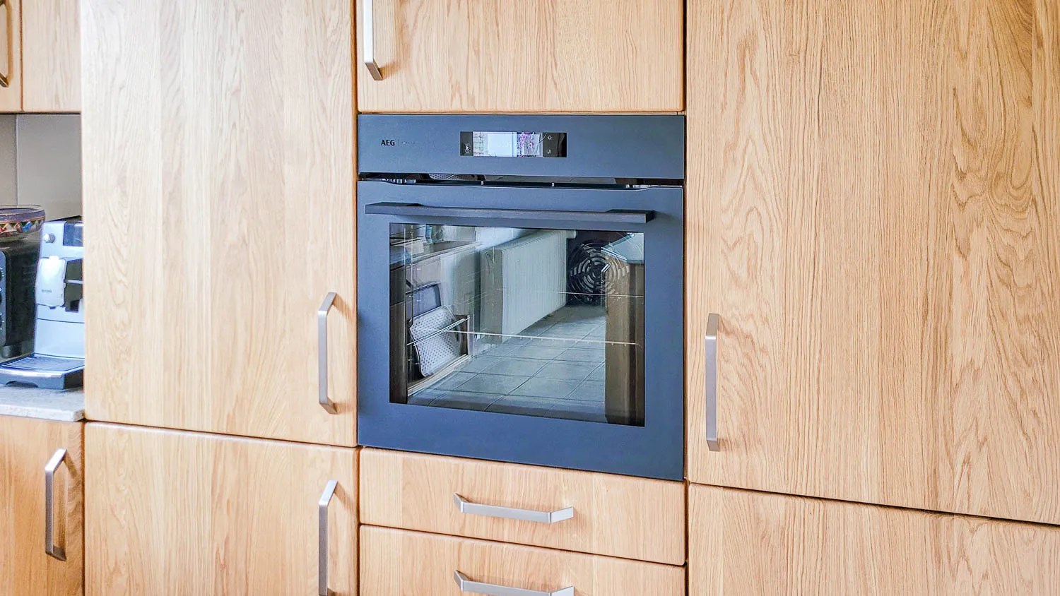 Einbau-Backofen in Hochschrankzeile aus heller Buche/Erle neben Kaffeevollautomat.