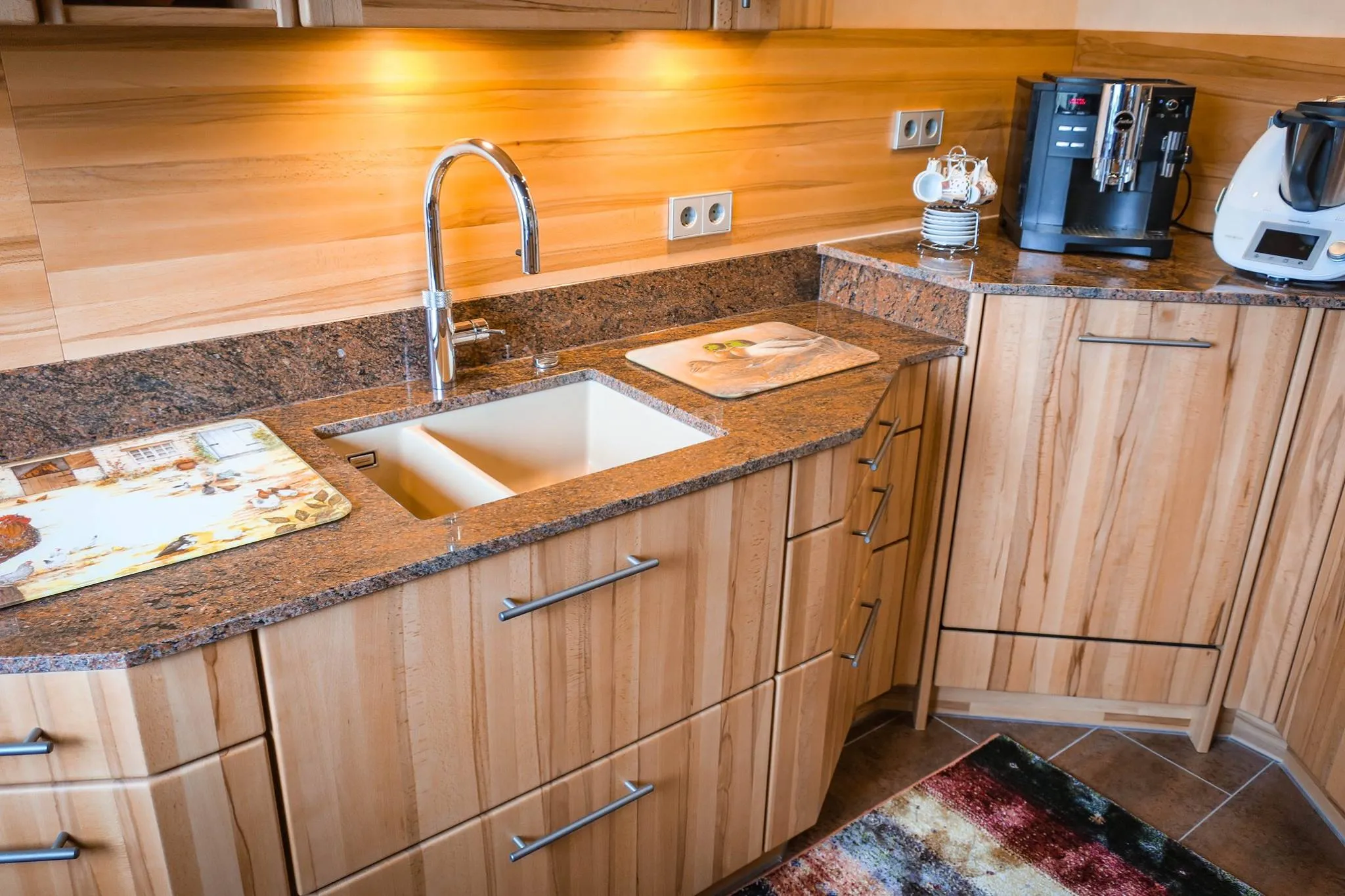 Eckbereich der Eichen-Küche mit Unterbau-Spüle und Bogenarmatur in Granit-Arbeitsplatte, Holz-Rückwand und Ecklösung mit gerundeter Eichen-Front