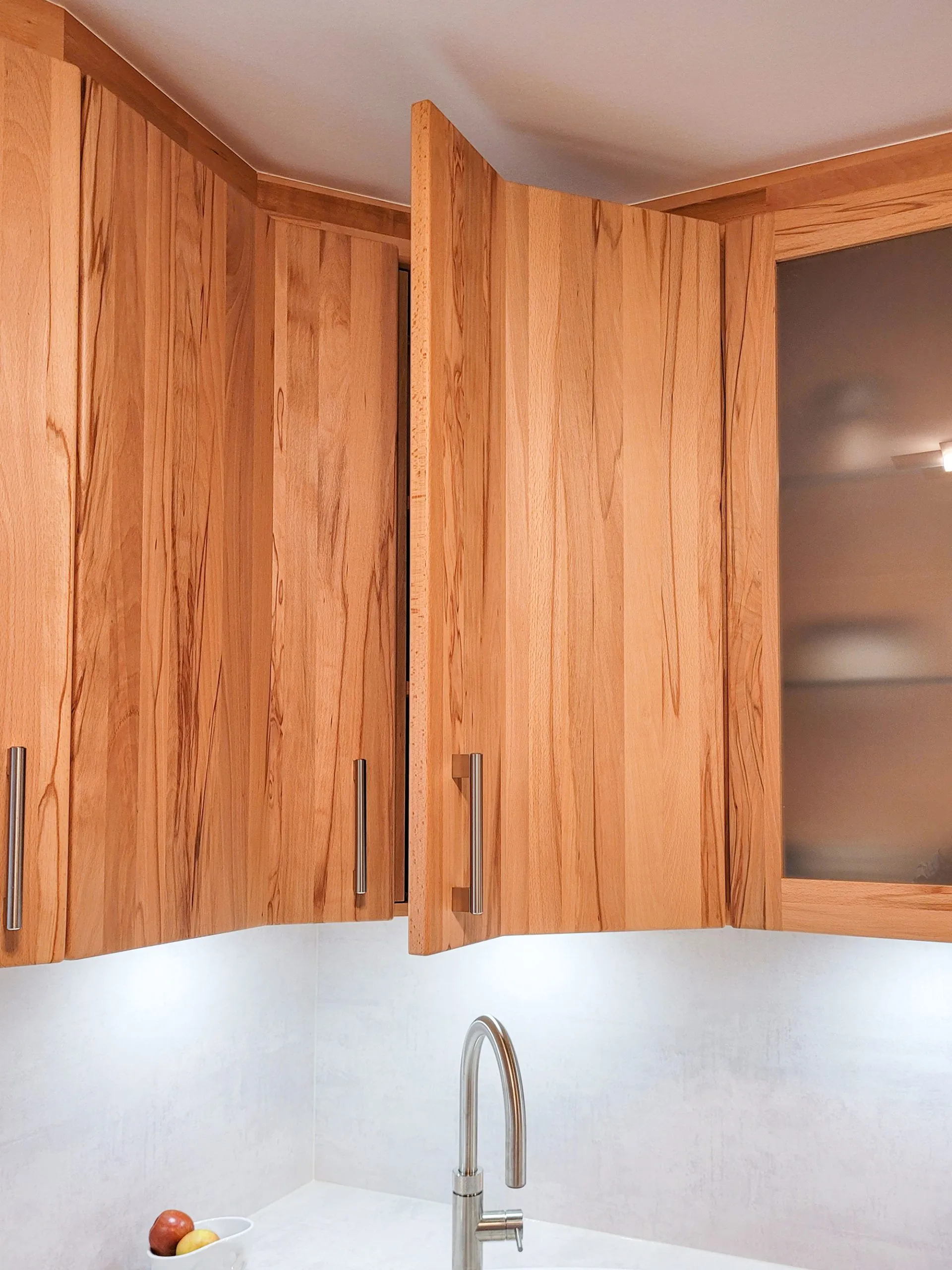 Eckbereich der Oberschränke aus Massivholz mit Glas-Eckvitrine über der Spüle.