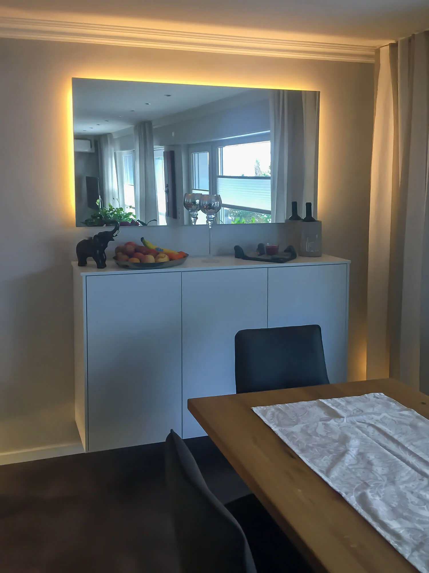 Sideboard mit indirekt beleuchtetem Wandspiegel und Esstisch im Wohnbereich