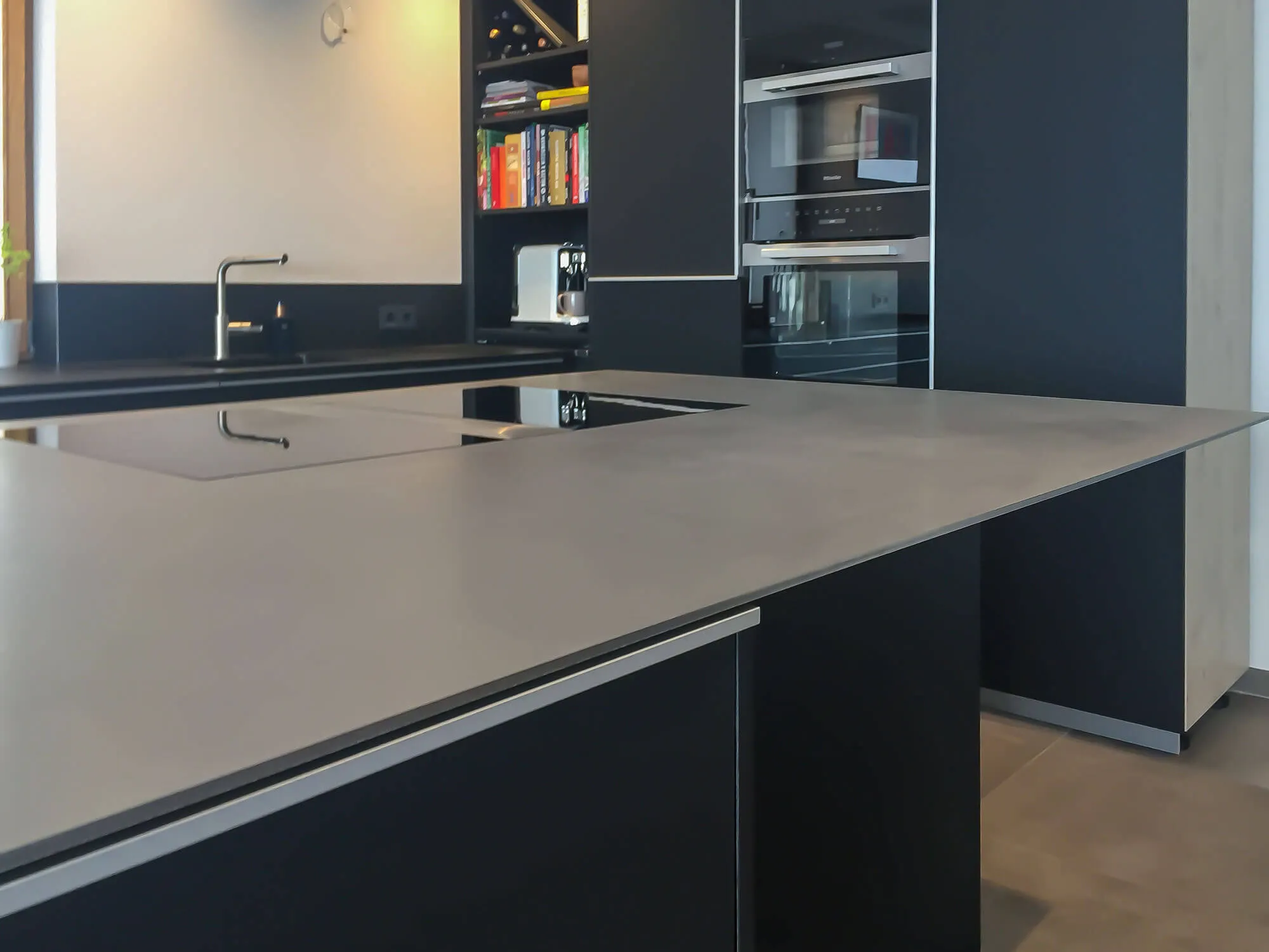 Moderne grifflose Inselküche in Anthrazit mit heller Steinarbeitsplatte und Hochschrankzeile mit Einbaugeräten