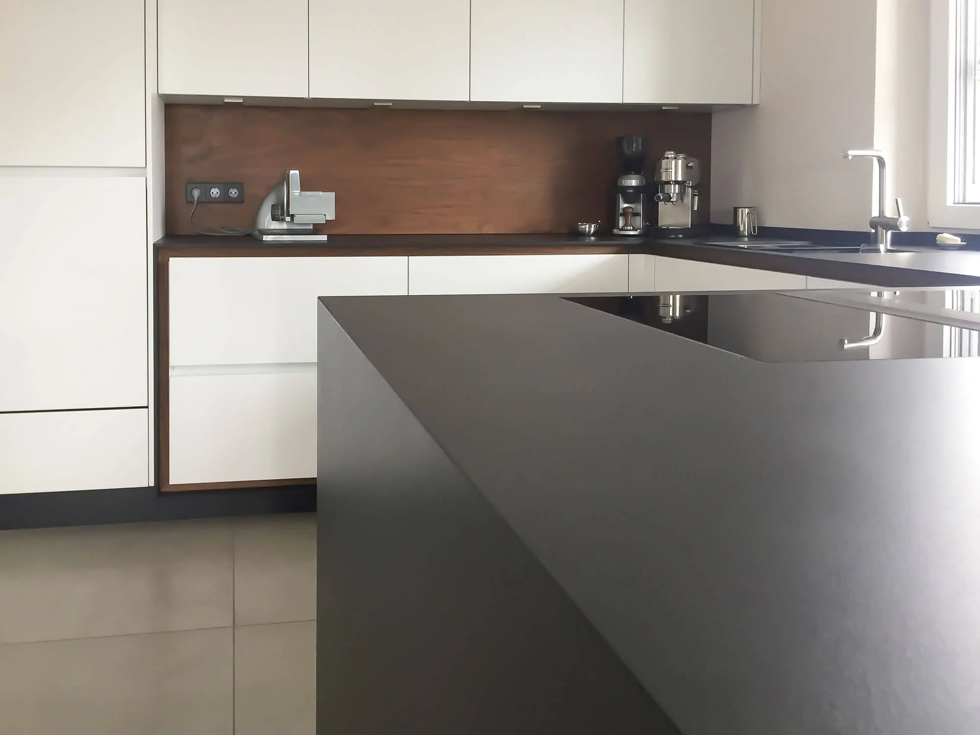 Grifflose weiße Küche mit markanter schwarzer Kochinsel in trapezförmigem Design