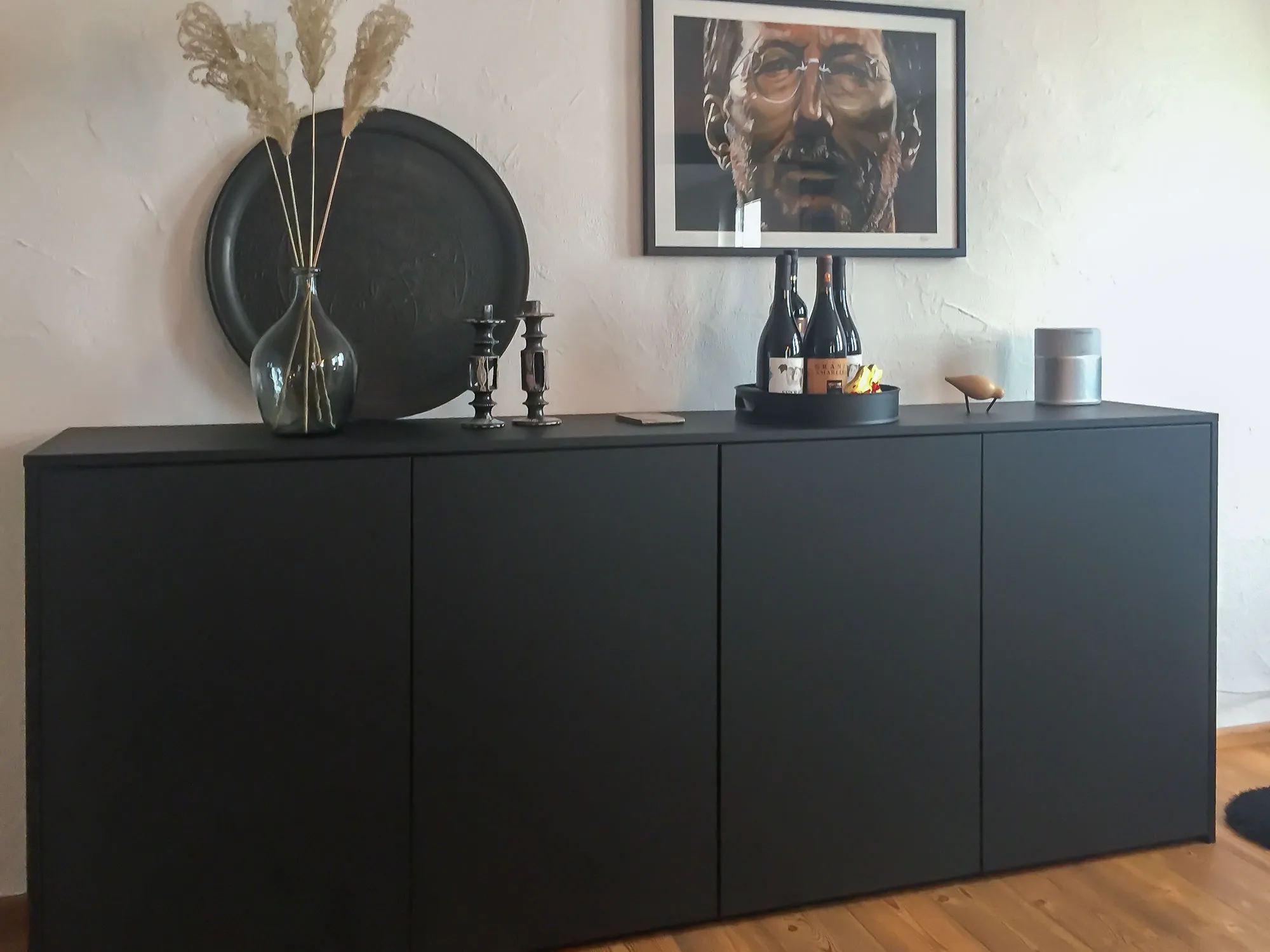 Schwarzes Sideboard im Wohnbereich mit Pampasgras-Vase, Kerzenleuchtern und Wanddeko