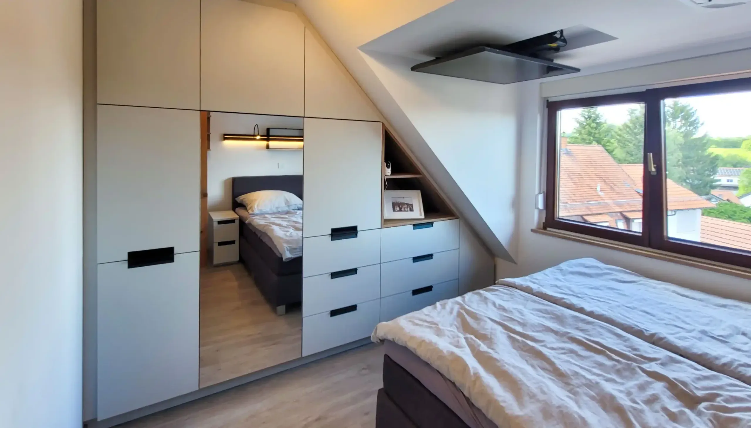 Dachgeschoss-Schlafzimmer mit Doppelbett, maßgefertigter Einbauschrankwand und Spiegelelementen.