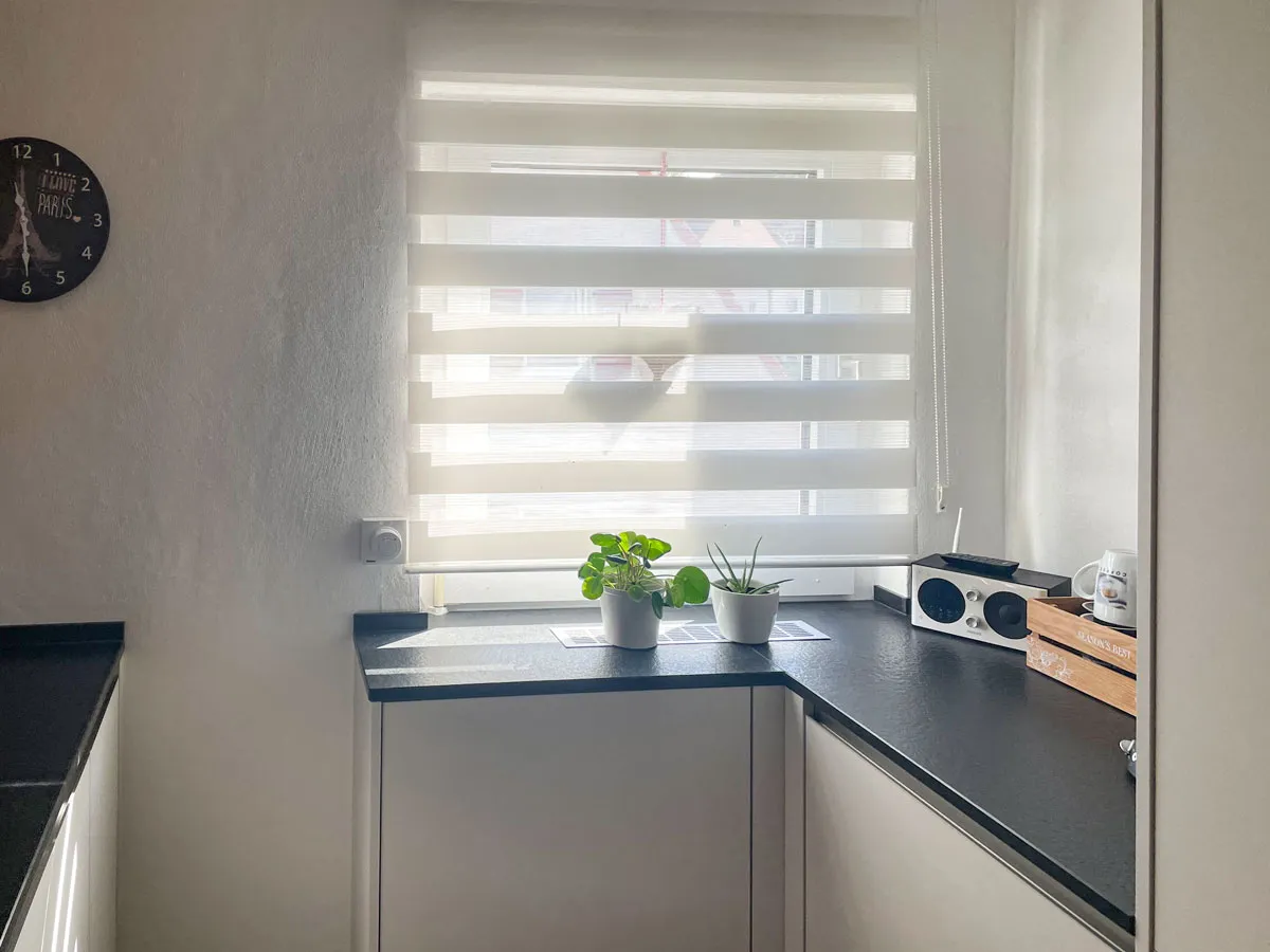 Küchen-Eckbereich am Fenster mit dunkler Arbeitsplatte, Pflanzen und Wanddeko