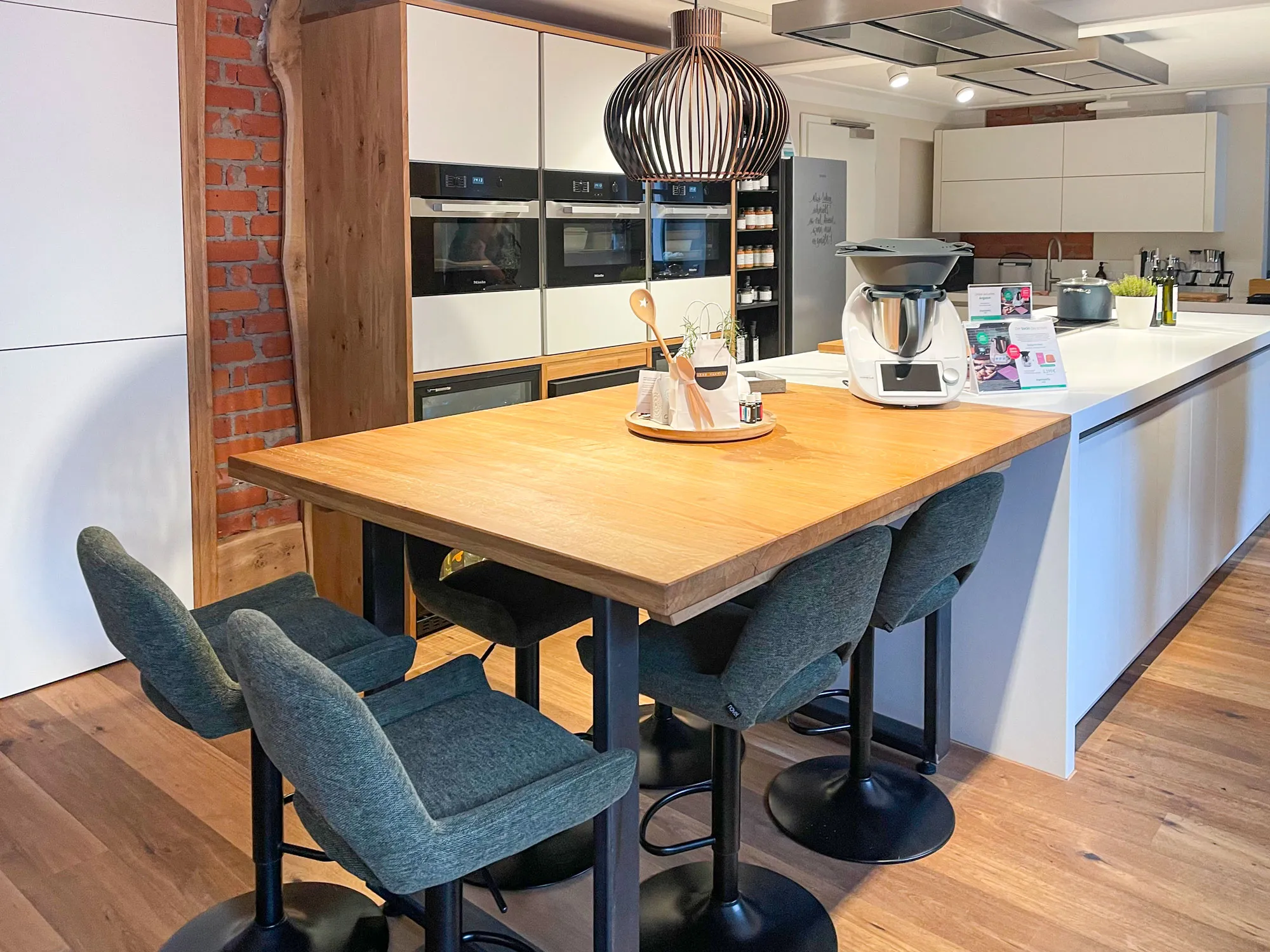 Holz-Esstheke mit Polster-Barhockern, Thermomix und kunstvoller Pendelleuchte