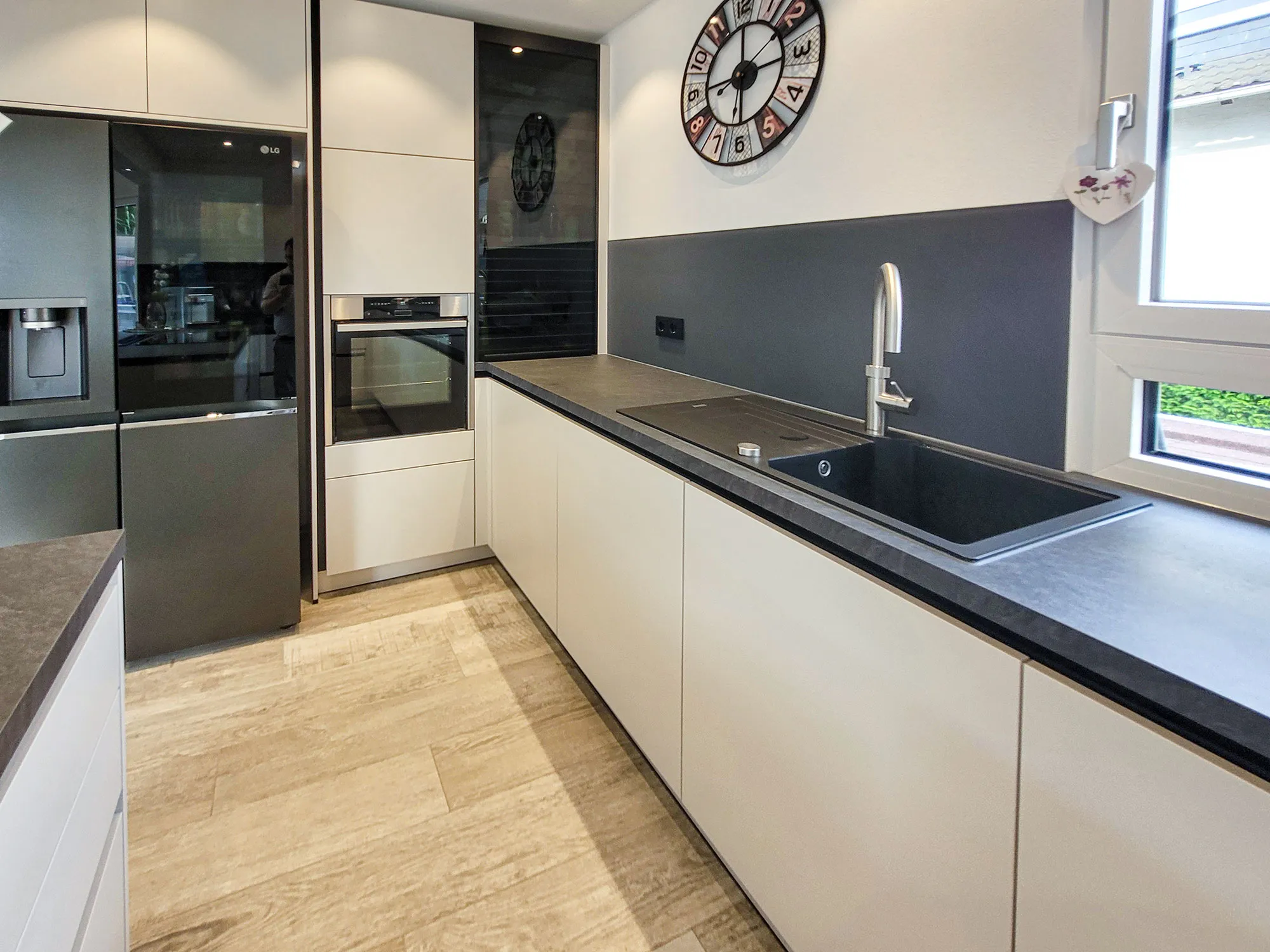 Weiße griffloses Zeilenküche mit dunkler Arbeitsplatte, Spüle, Backofenturm und Side-by-Side-Kühlschrank.