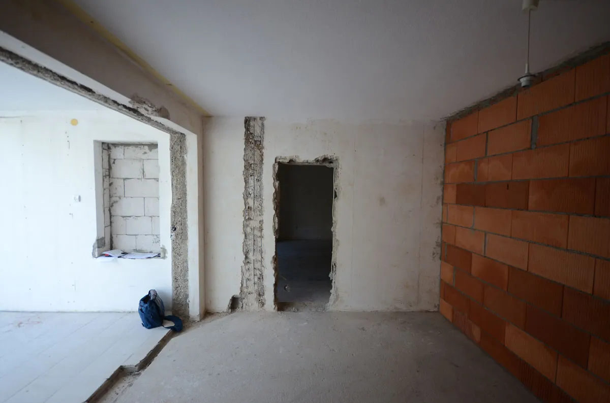 Rohbauraum mit Ziegelwand rechts und Türöffnungen zu Nebenräumen, gespachtelte Wände und Betonboden – vor der Modernisierung durch Broßler Küche Aktiv