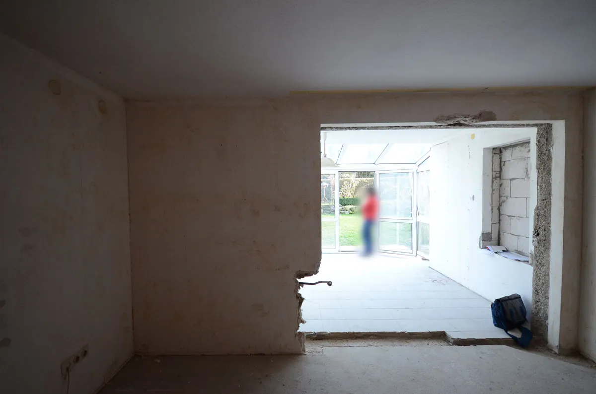 Rohbauraum mit Wanddurchbruch und Blick in einen hellen Nebenraum mit Glasfassade, gespachtelte Wände und Betonboden – vor der Modernisierung durch Broßler Küche Aktiv