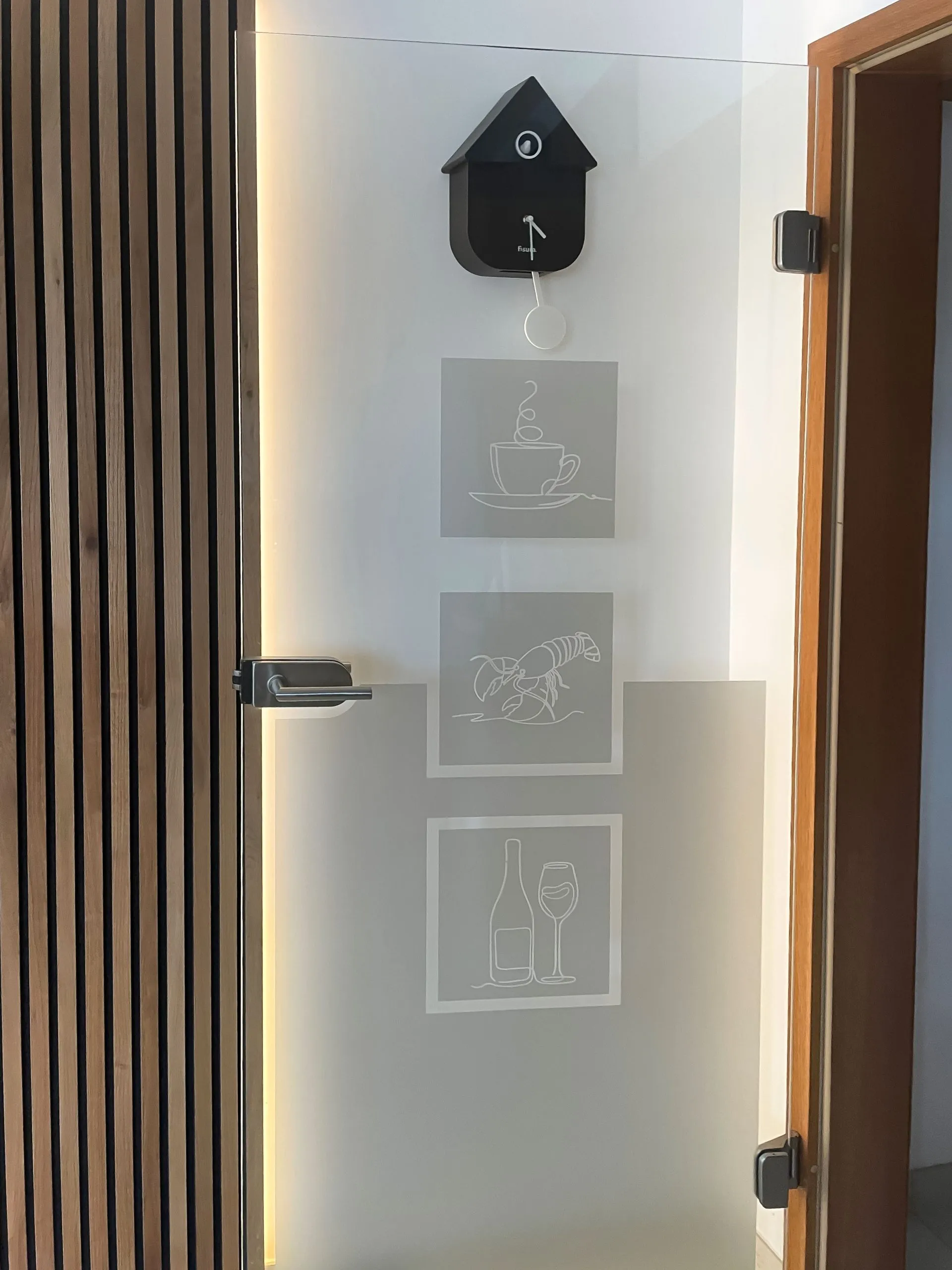 Mattierte Glas-Schiebetür mit gravierten Küchen-Motiven vor Holzlamellen-Wand