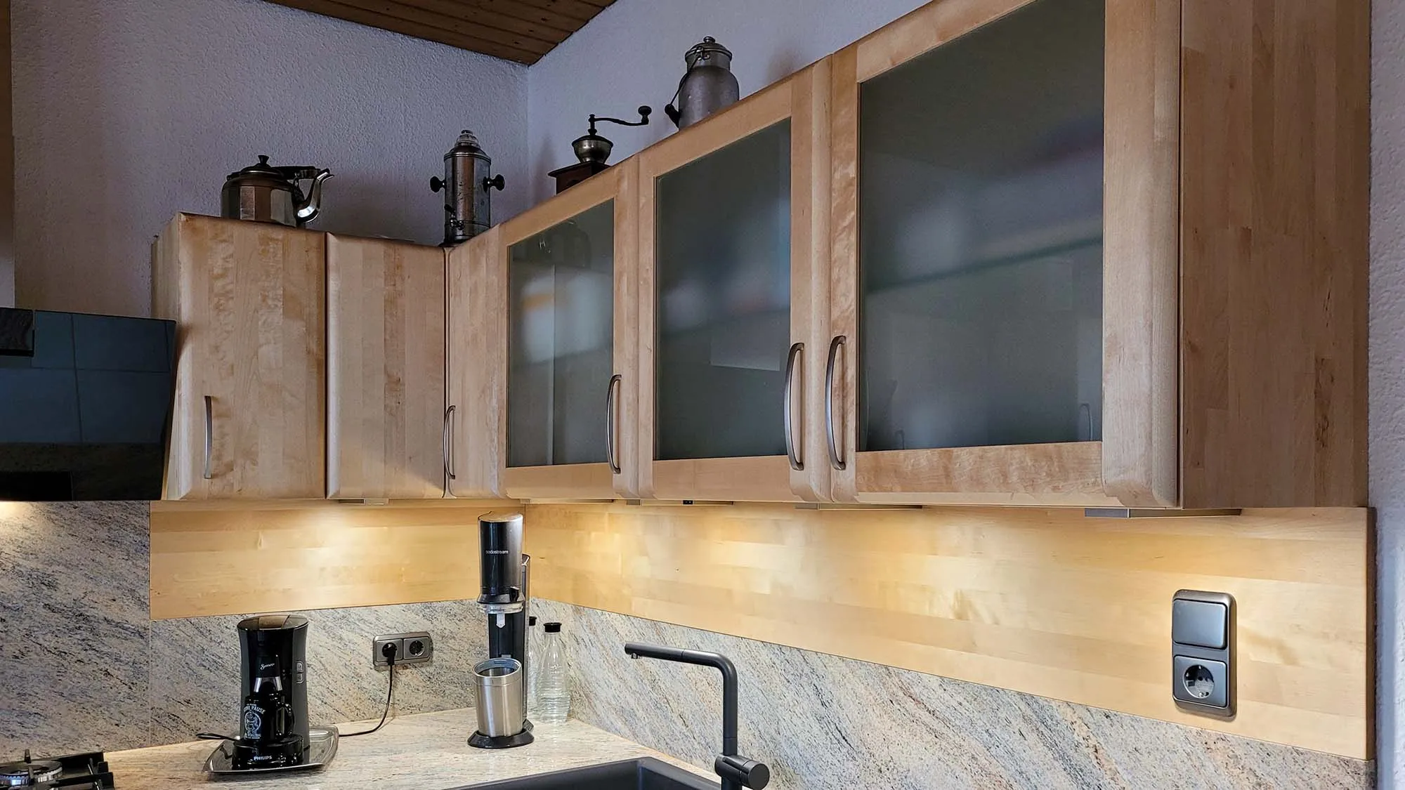 Detail Glas-Hängeschränke in Eiche mit antiken Kupferkannen oben, Granit-Rückwand mit eingebauten Steckdosen, Spüle und Kaffeemaschine in der Arbeitszeile