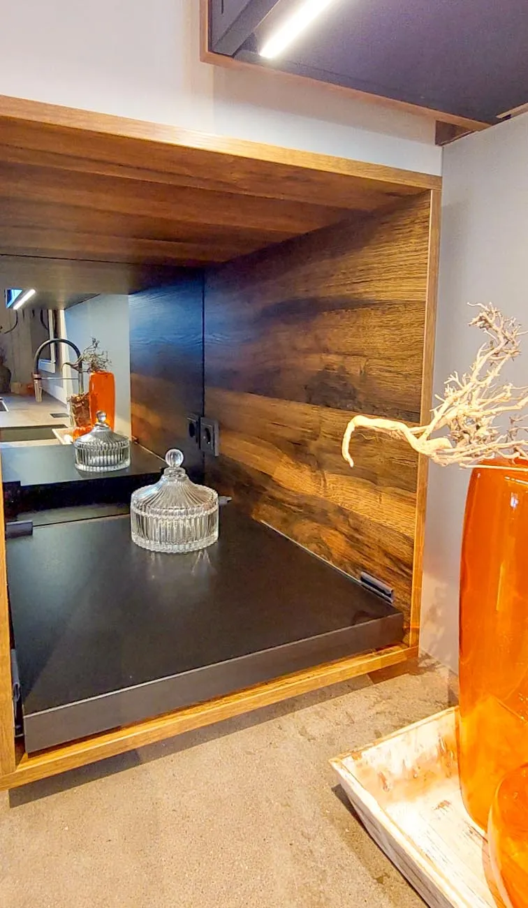 Holznische in der Küche mit Spiegel-Rückwand und dunkler Ablagefläche, dekoriert mit Glasdose, oranger Glasvase und Treibholz – im Spiegel reflektiert sich der Spülbereich