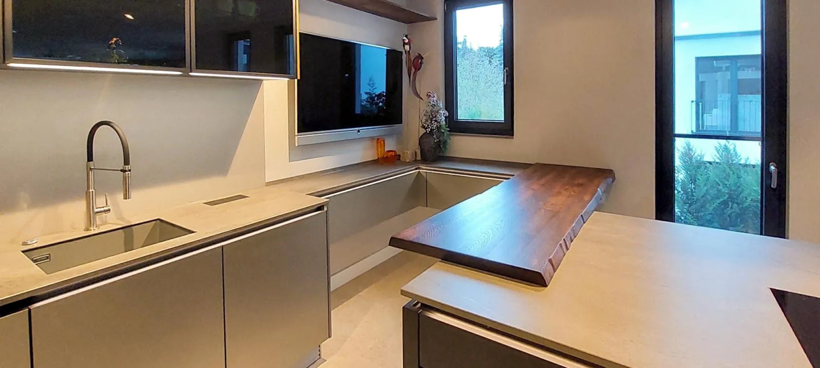 Spülbereich am Fenster mit Bogenarmatur und Unterbau-Spüle, anthrazitgraue Unterschränke, dunkelgraue Steinarbeitsplatte und angesetzte Holz-Bartheke aus Massivholz mit Baumkante