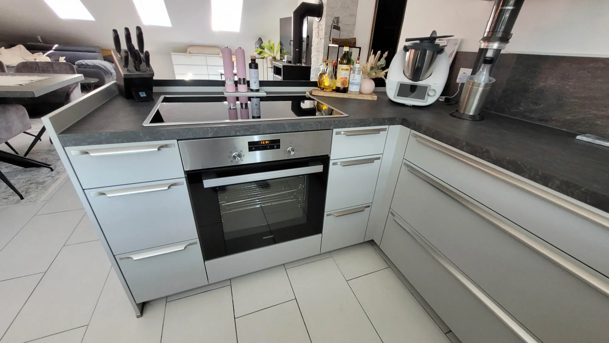 Detail Kochbereich mit Backofen-Einbau in Unterschrank, Induktionskochfeld mit Muldenlüfter, Edelstahl-Griffleisten und anthrazitfarbener Arbeitsplatte
