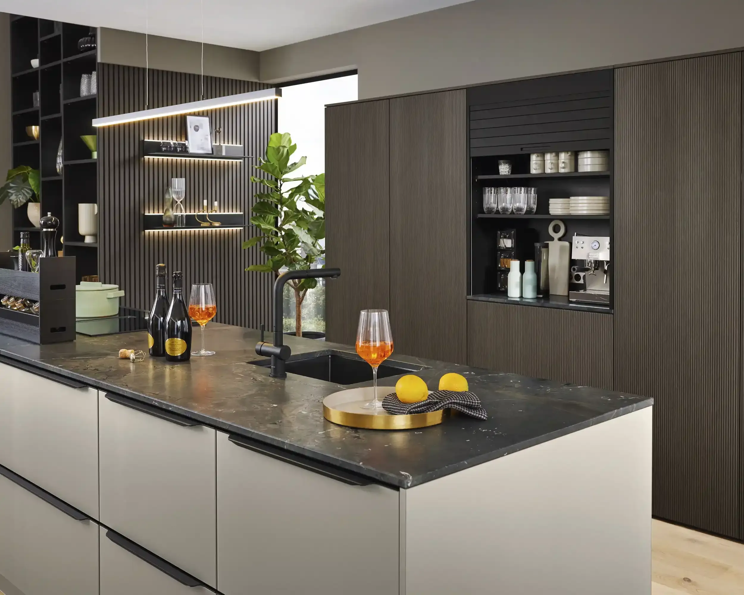 Kücheninsel in Taupe mit dunkler Steinarbeitsplatte, Aperitif-Setting und geriffelter Holz-Rückwand mit Bar