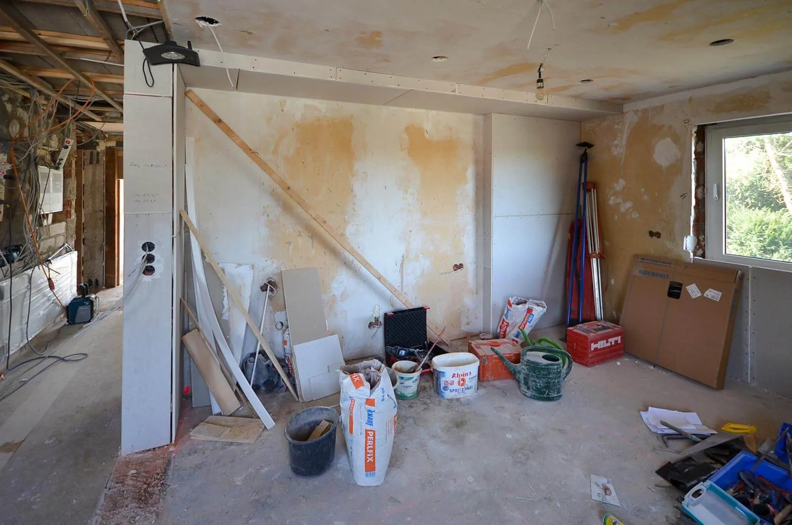 Vorher-Aufnahme eines entkernten Rohbauraums vor dem Kücheneinbau, freigelegte Altputz-Wände, sichtbare Holzstützen und Träger, Baumaterial und Werkzeug im Raum, zwei Fenster sorgen für Tageslicht – Ausgangssituation für eine Küchenplanung von Dietmar Kraus bei Broßler Küche Aktiv