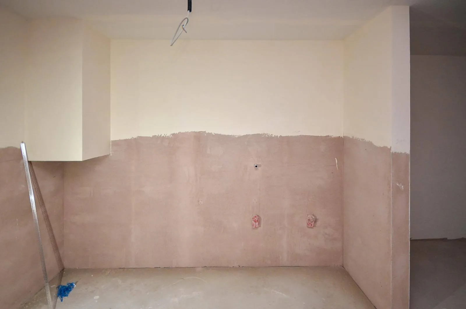 Vorher-Aufnahme einer Nische im Rohbau vor dem Kücheneinbau, frisch verputzte Wände mit rosa Grundierung, vorbereitete Anschlüsse für Strom und Wasser, Estrich-Boden – Ausgangssituation für eine Küchenplanung von Dietmar Kraus bei Broßler Küche Aktiv