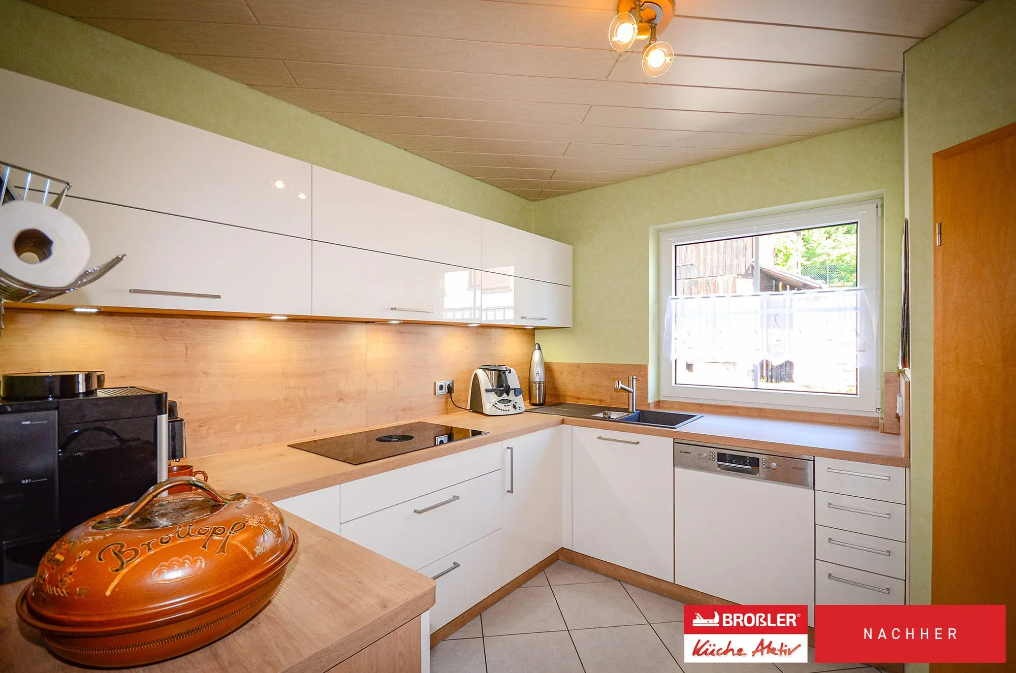 Nachher-Aufnahme: grifflose weiße U-Küche mit Massivholz-Arbeitsplatte, Holz-Nischenrückwand und grüner Wand.
