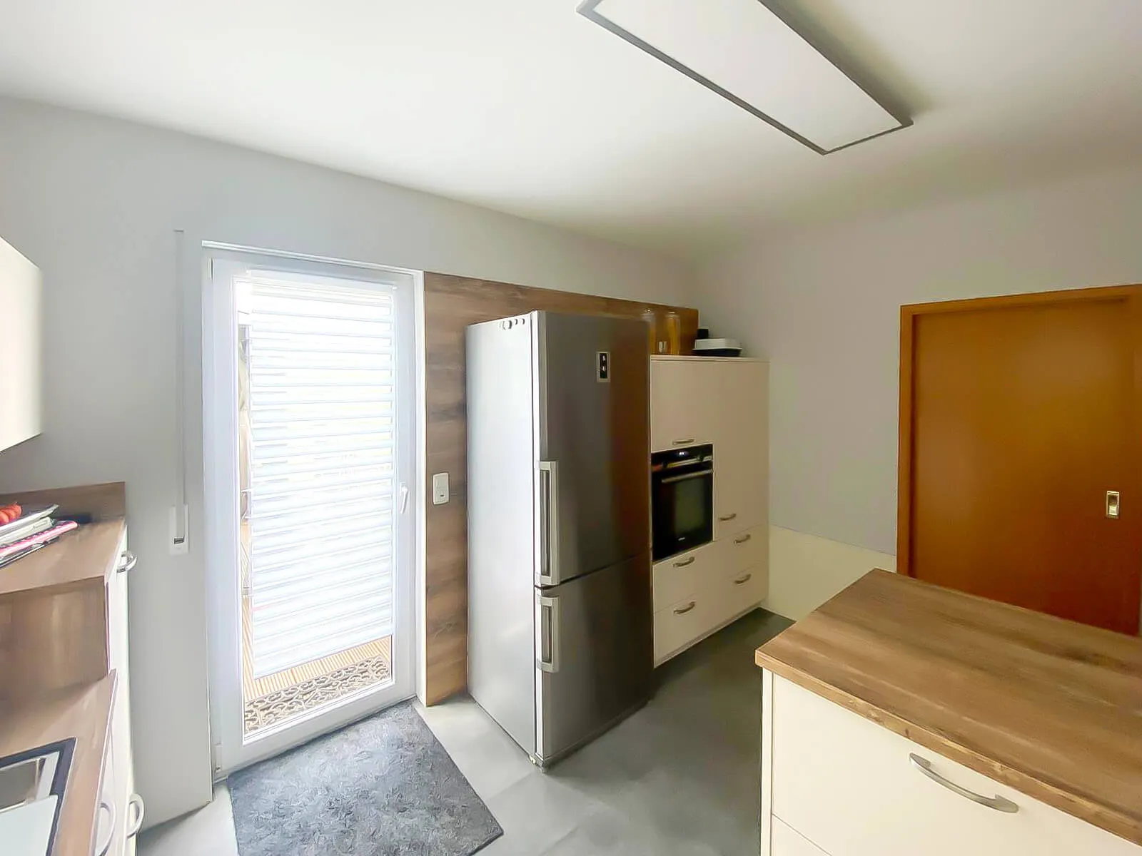 Küchenbereich mit freistehendem Kühlschrank, eingebautem Backofen und Terrassentür