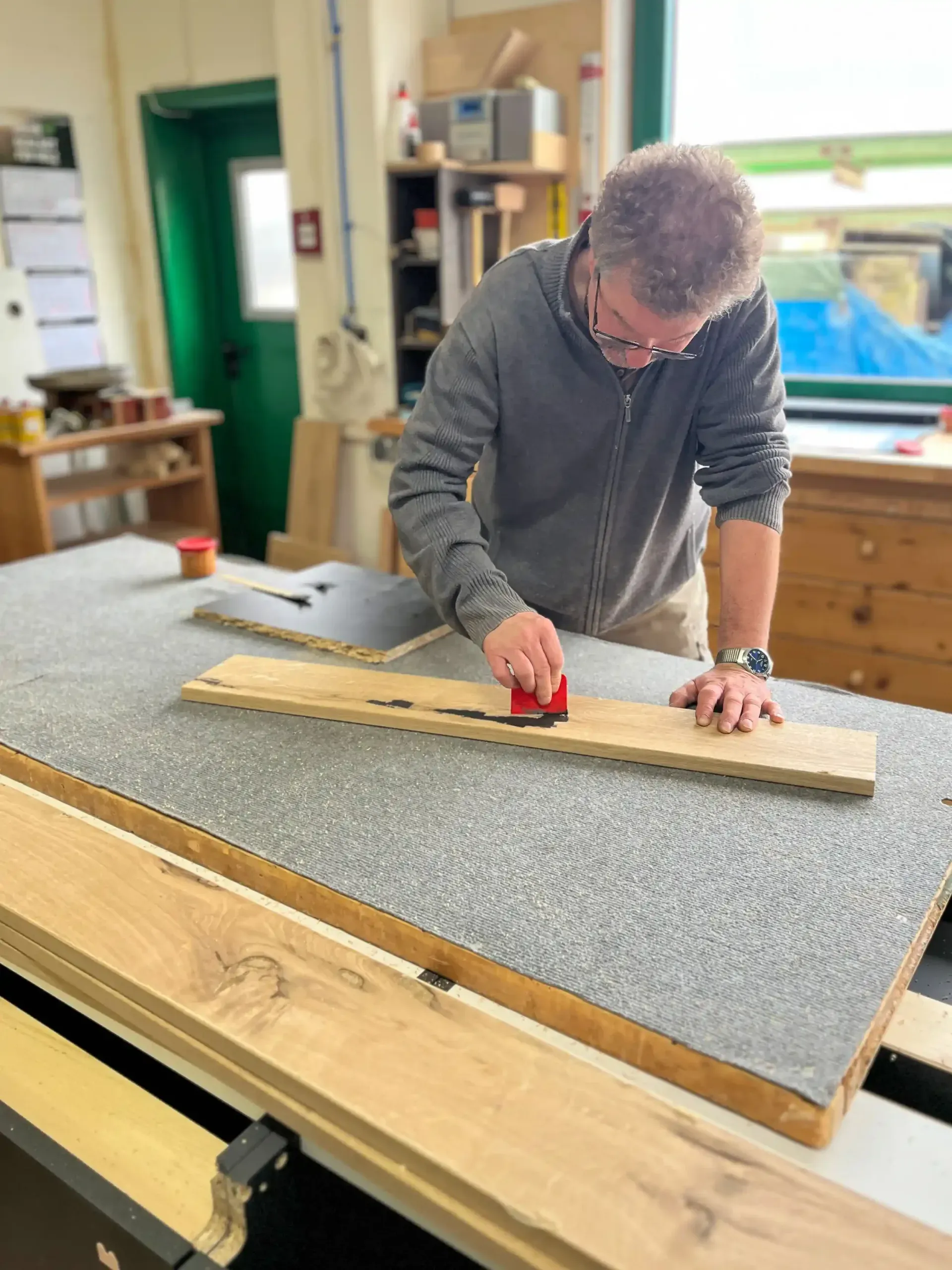 Handwerker in einer Schreinerei-Werkstatt bei der Vorbereitung von massiven Holzelementen für eine maßgefertigte Küche, mit Werkzeug an einem Holzbrett arbeitend – Fertigung einer Küche von Broßler Küche Aktiv (Standort Ehrbach/Großheubach)