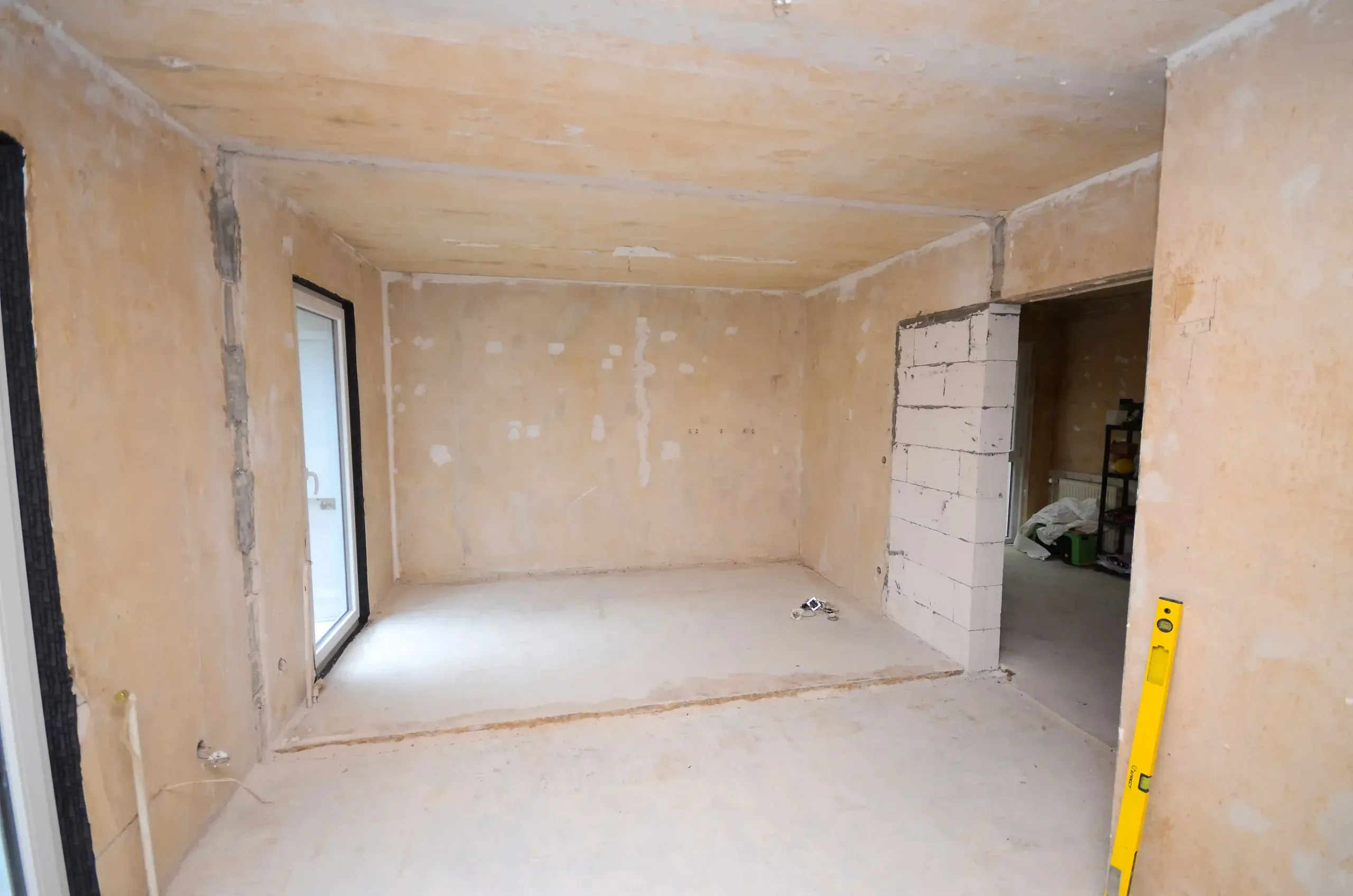 Großer Rohbauraum mit bodentiefer Fenstertür links, gespachtelten Wänden, Estrichboden und Wasserwaage im Vordergrund – vor der Modernisierung durch Broßler Küche Aktiv (Standort Ehrbach/Großheubach)