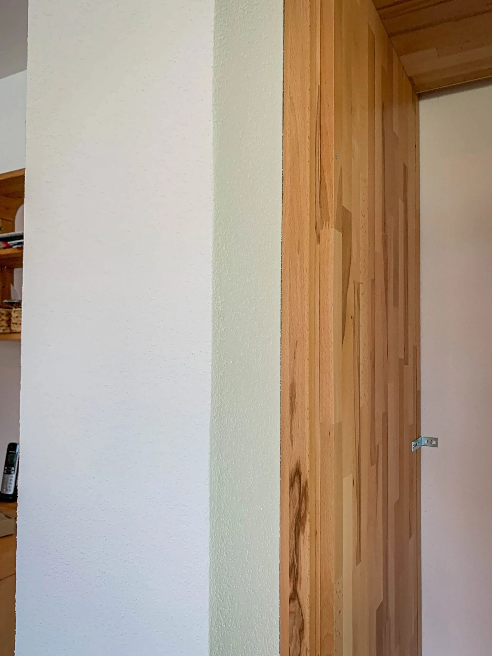 Detailaufnahme einer Massivholz-Hochschrank-Seitenwange vor weißer Wand während der Küchenmontage.