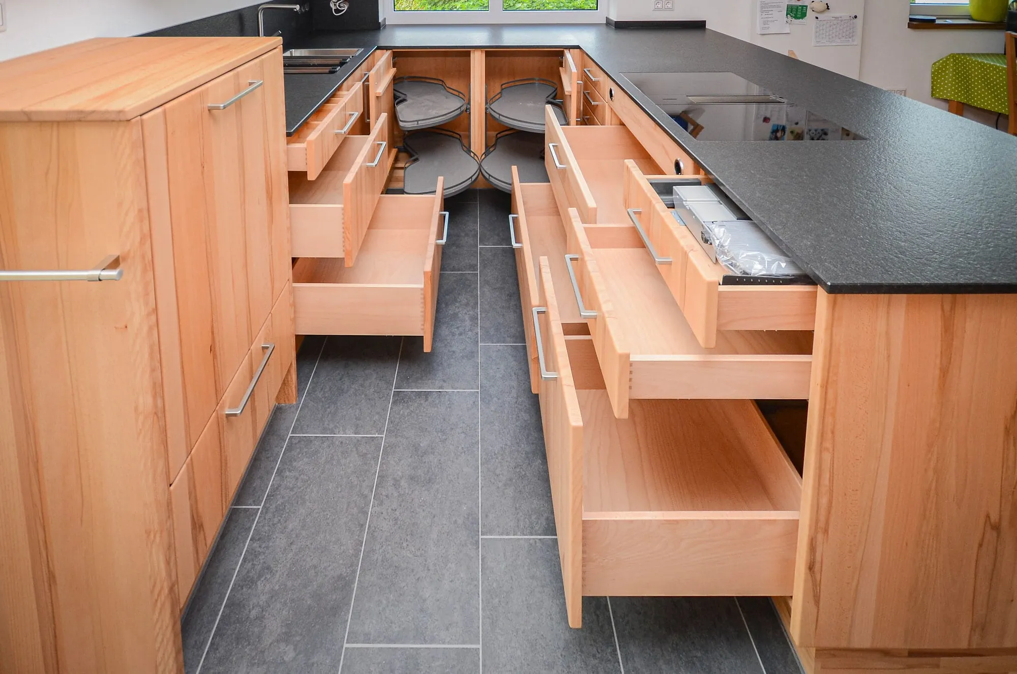 Detailaufnahme der Innenorganisation einer Massivholz-Kochinsel mit ausgezogenen Schubladen und Eckkarussells.