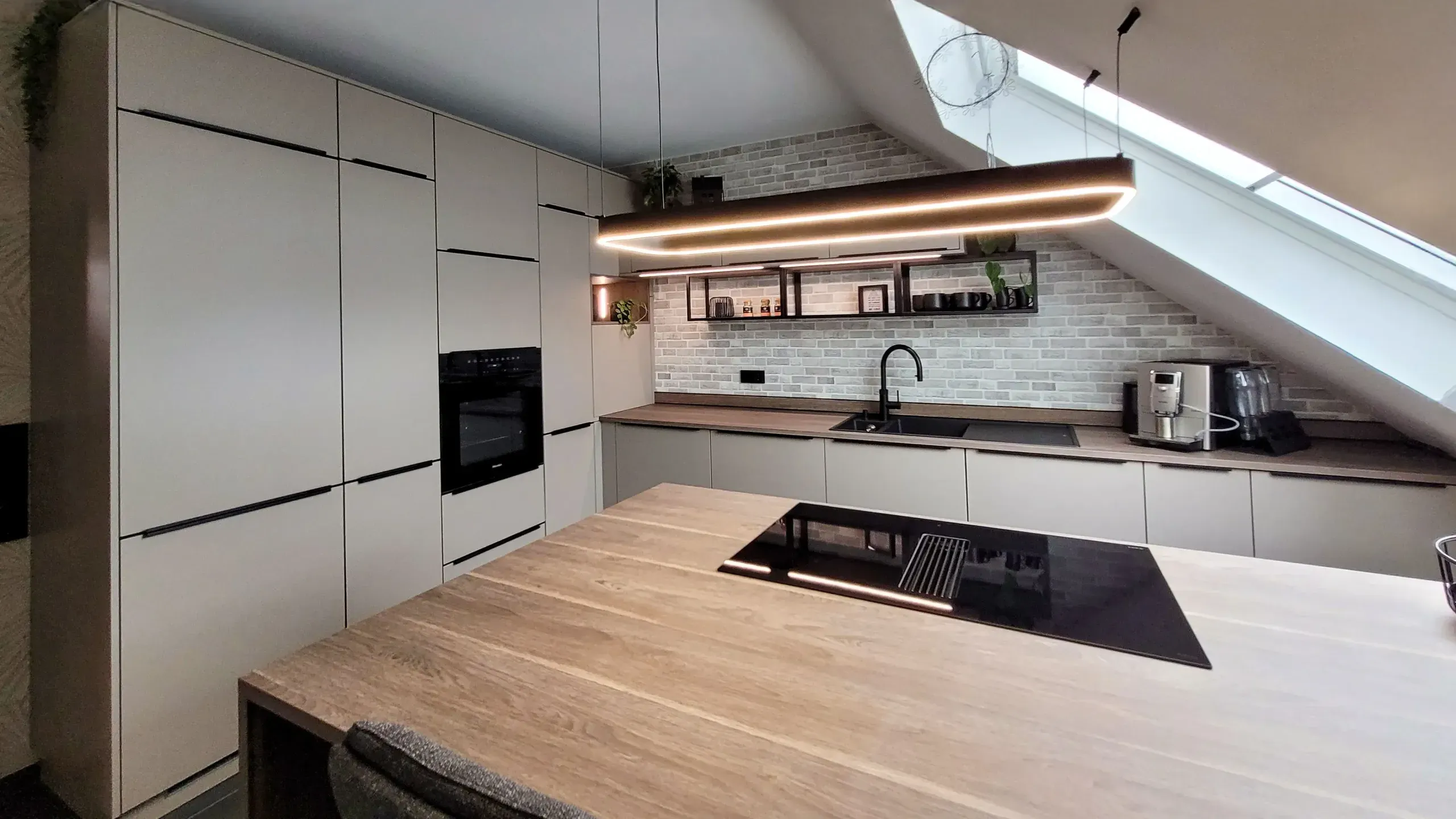 Blick über die Holzkochinsel zur Wandzeile mit Hochschränken, Spüle und schwebenden Regalen.