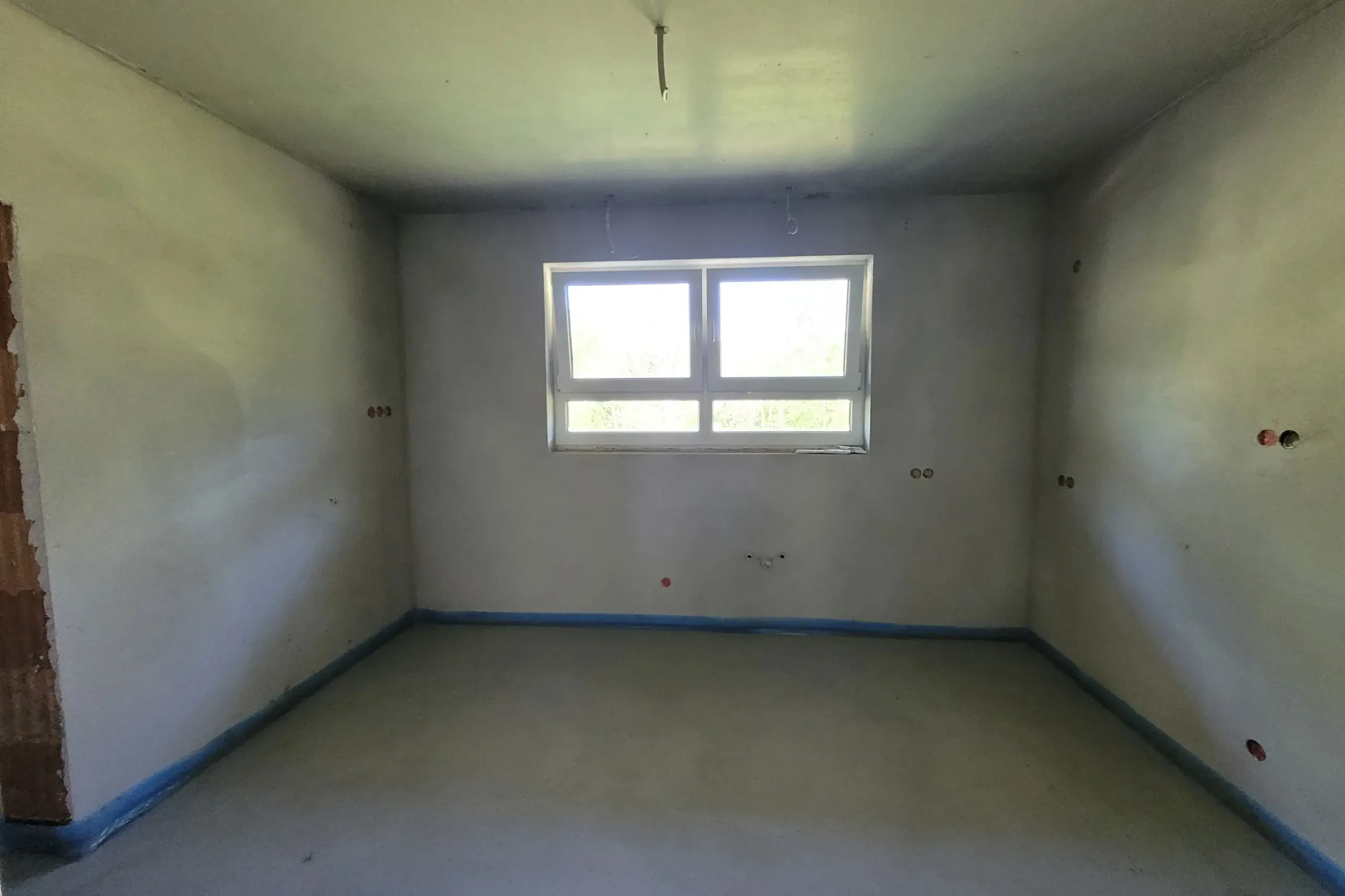 Leerer Rohbau mit Putzwänden, Estrich und zweigeteiltem Fenster als Ausgangsbasis der Küchenplanung.