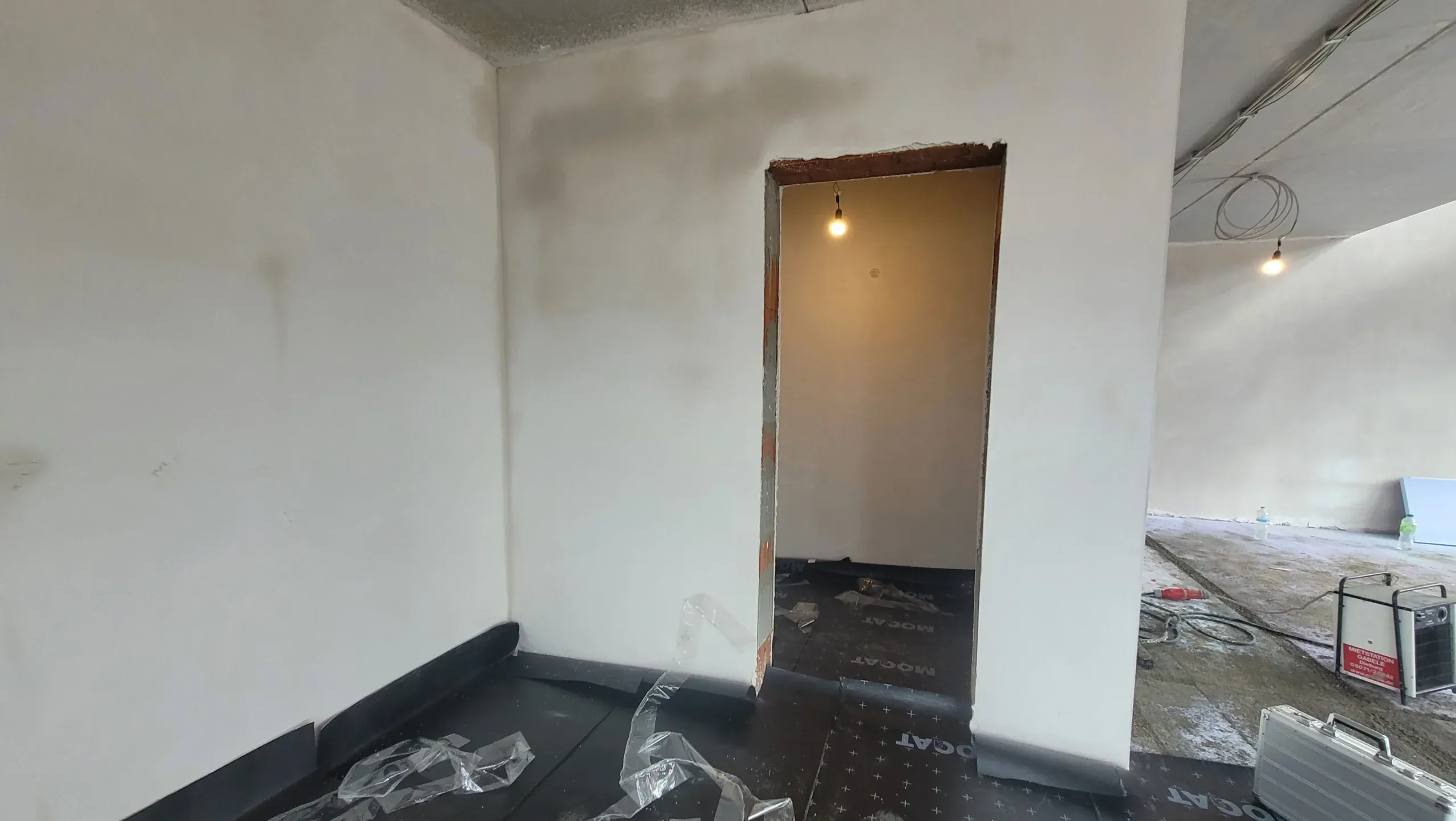 Vorher-Aufnahme im Rohbauzustand: leerer Raum mit Türöffnung, Bauschutz und losen Stromleitungen.