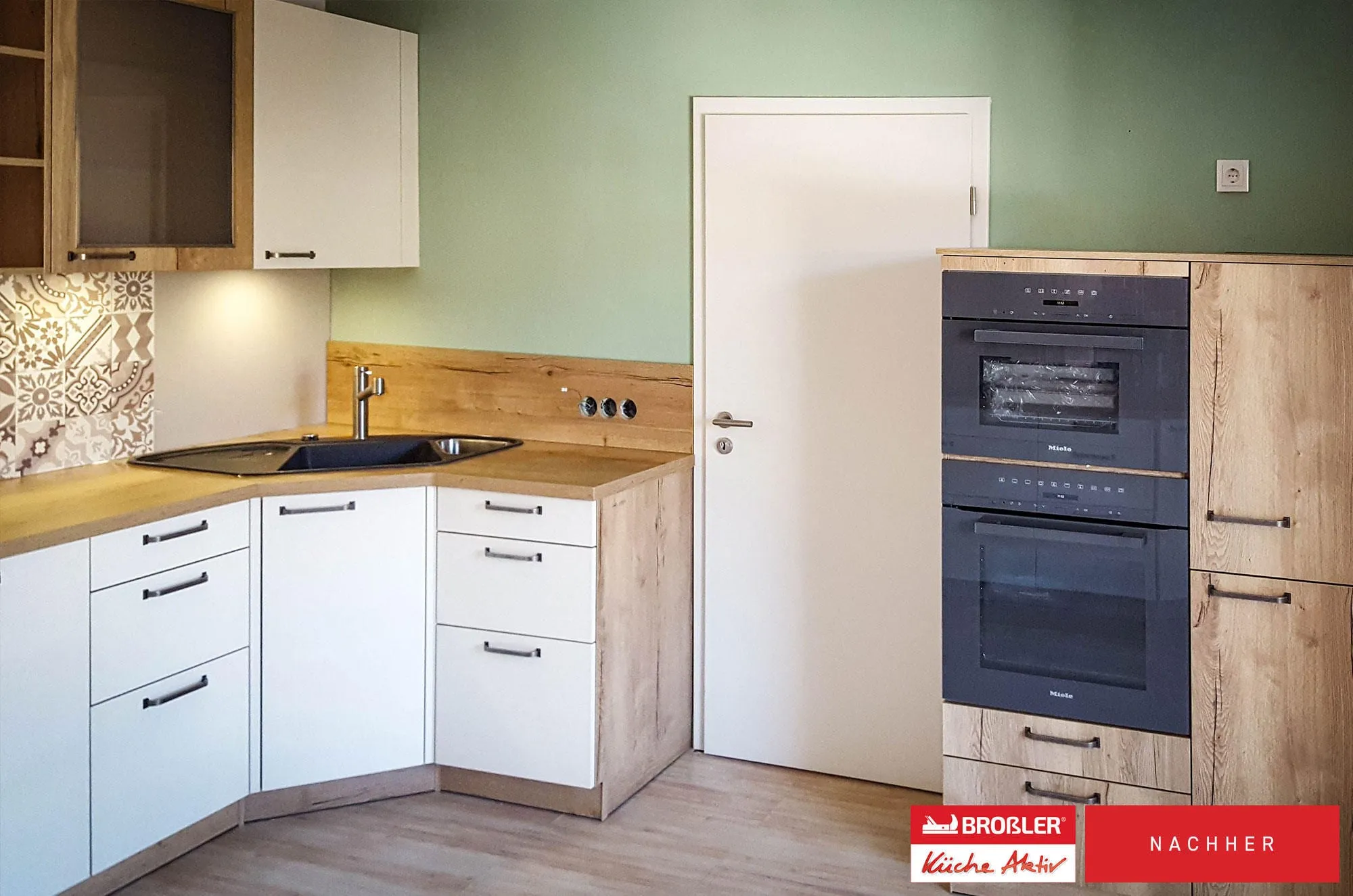 Nachher-Aufnahme: weiße L-Küche mit Eckspüle, Mosaik-Fliesenspiegel und Hochschrank mit Doppel-Backofen in Holzoptik.