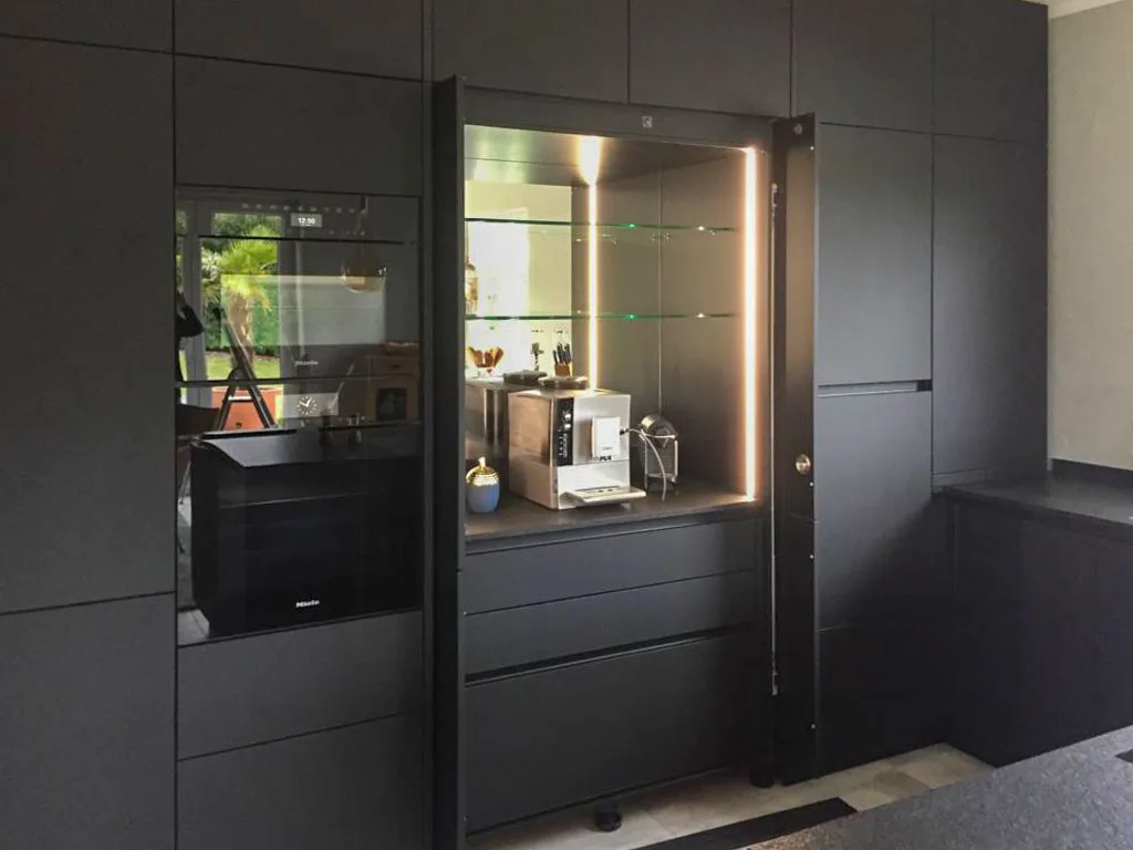 Beleuchtete Glasvitrine zwischen anthrazitfarbenen Hochschränken mit Espressomaschine und Miele-Backofen