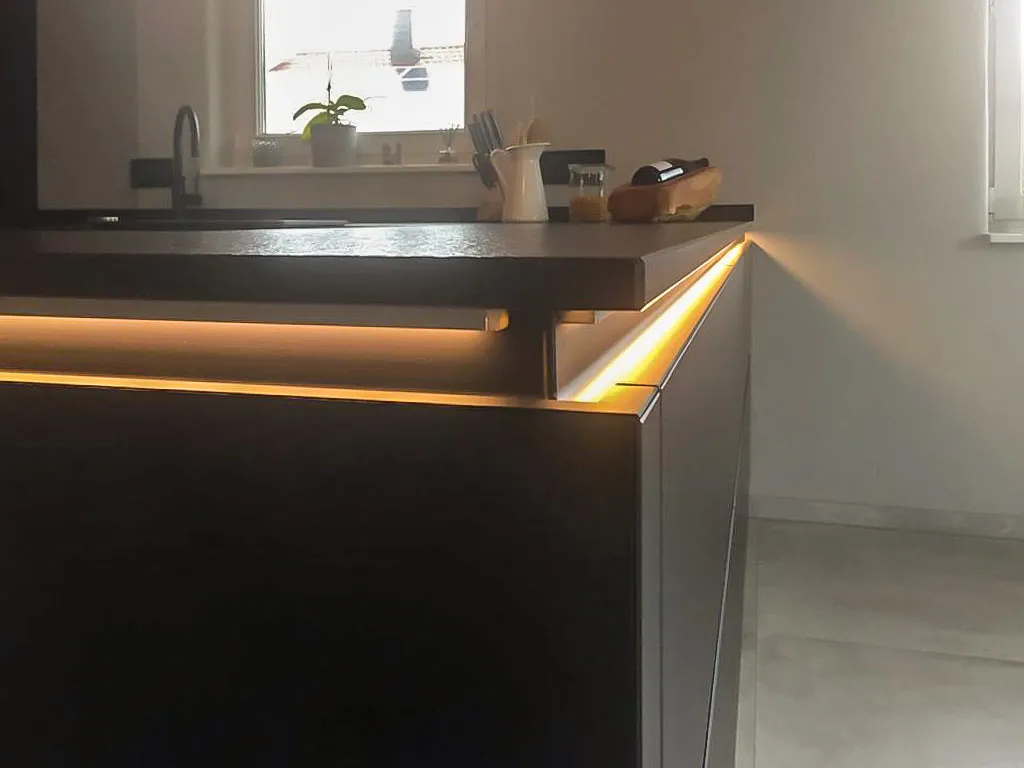 Eckdetail der Kücheninsel mit warmer LED-Beleuchtung unter der Arbeitsplatte