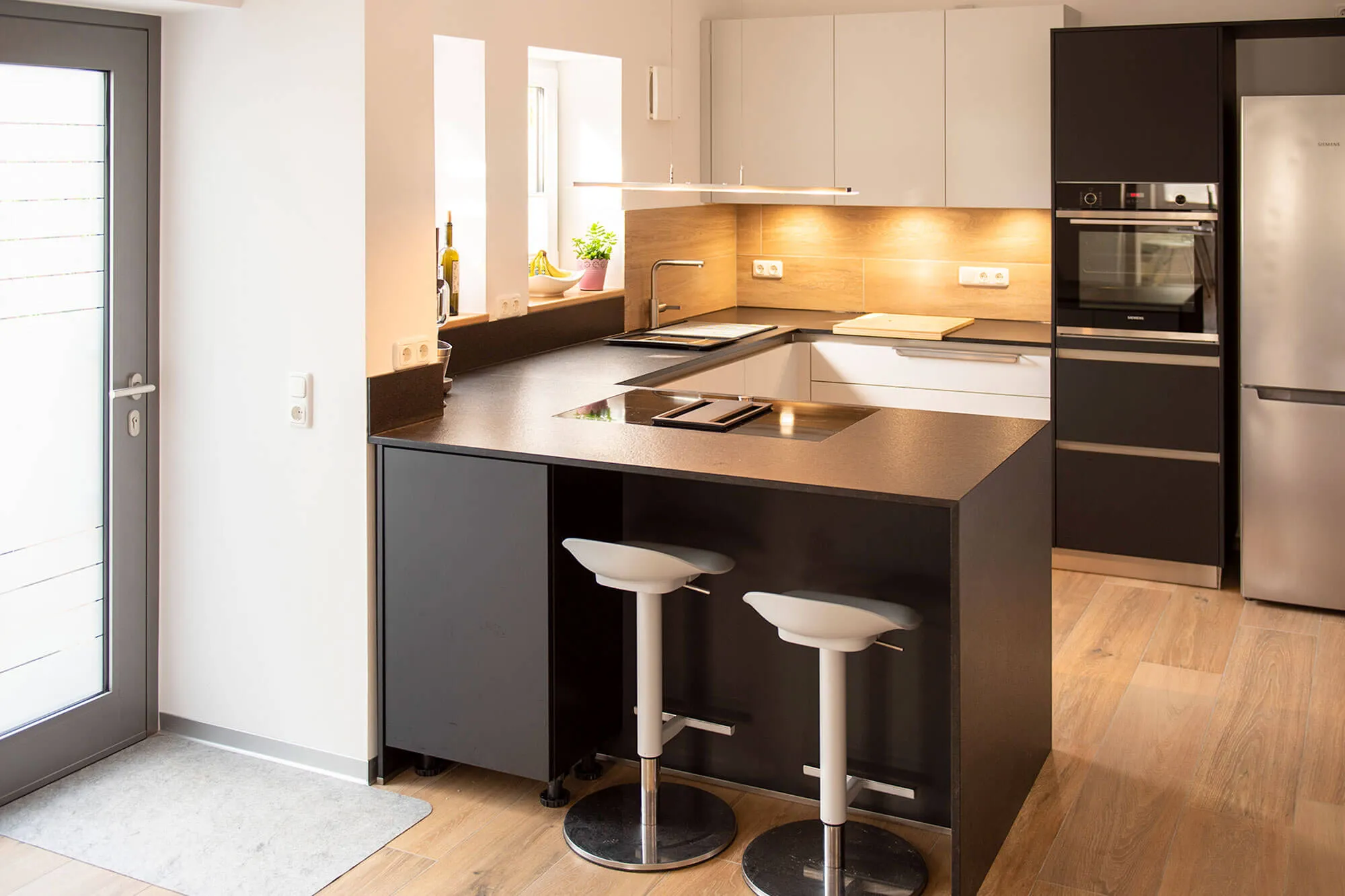 U-Küche mit dunkler Theke, weißen Designer-Barhockern und Holz-Nischenrückwand