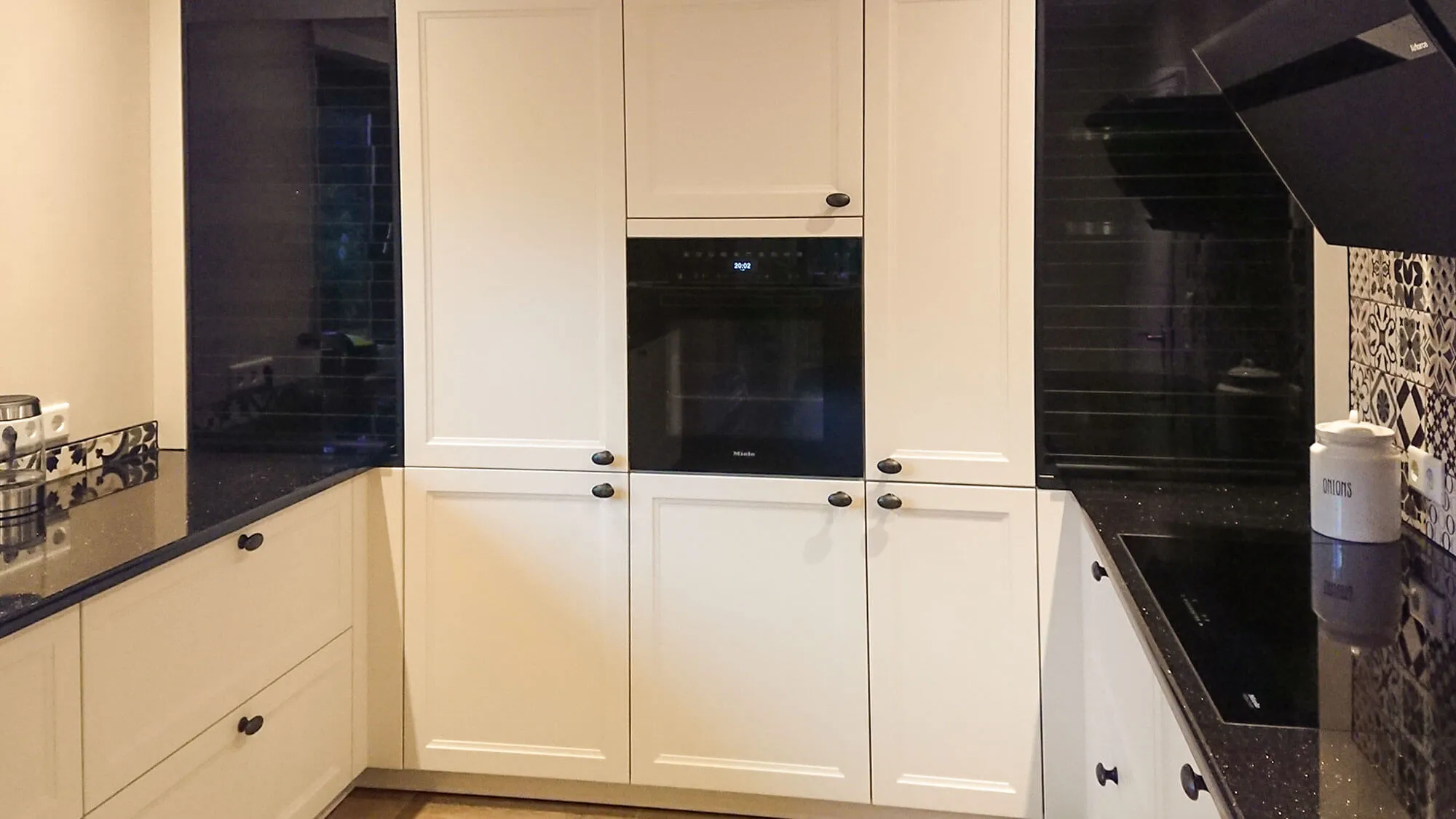 Landhaus-Küche mit eingebautem Miele-Backofen, dunkler Arbeitsplatte und Patchwork-Spritzschutz