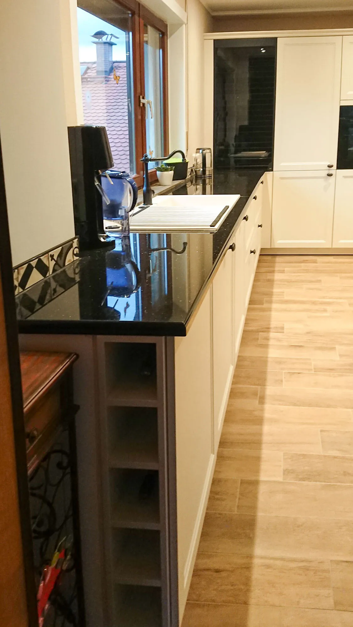 Halbinsel-Stirnseite mit dunkler Granitarbeitsplatte, offenem Sockel-Regal und Espressomaschine