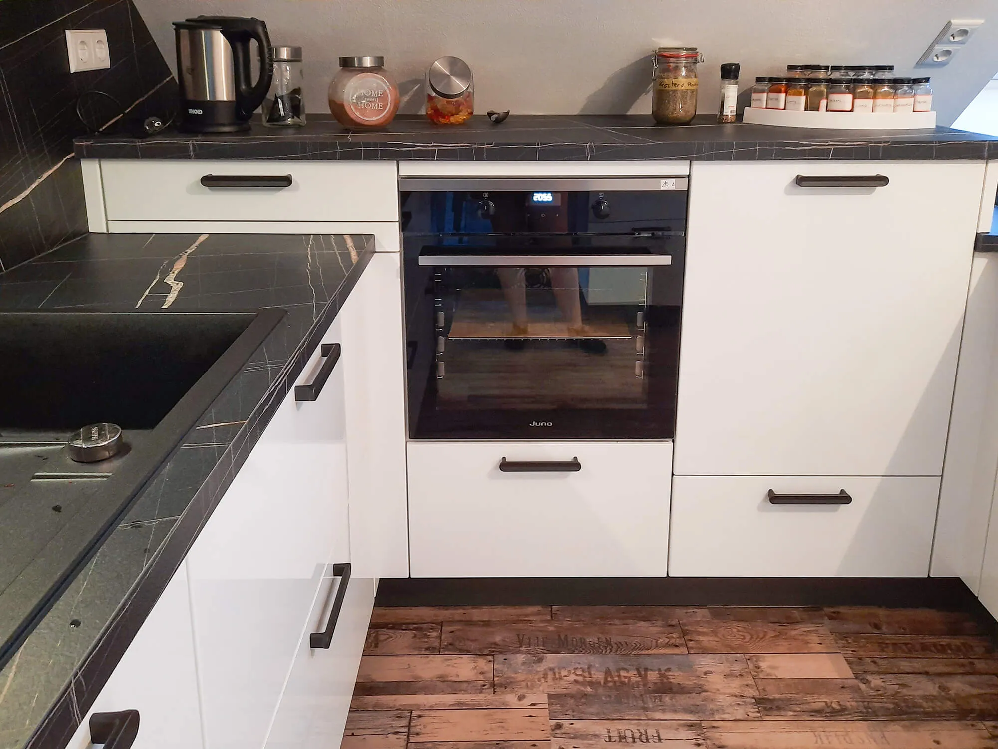 Eckansicht mit eingebautem Backofen, Marmor-Arbeitsplatte, Spüle und Vintage-Holzdielen