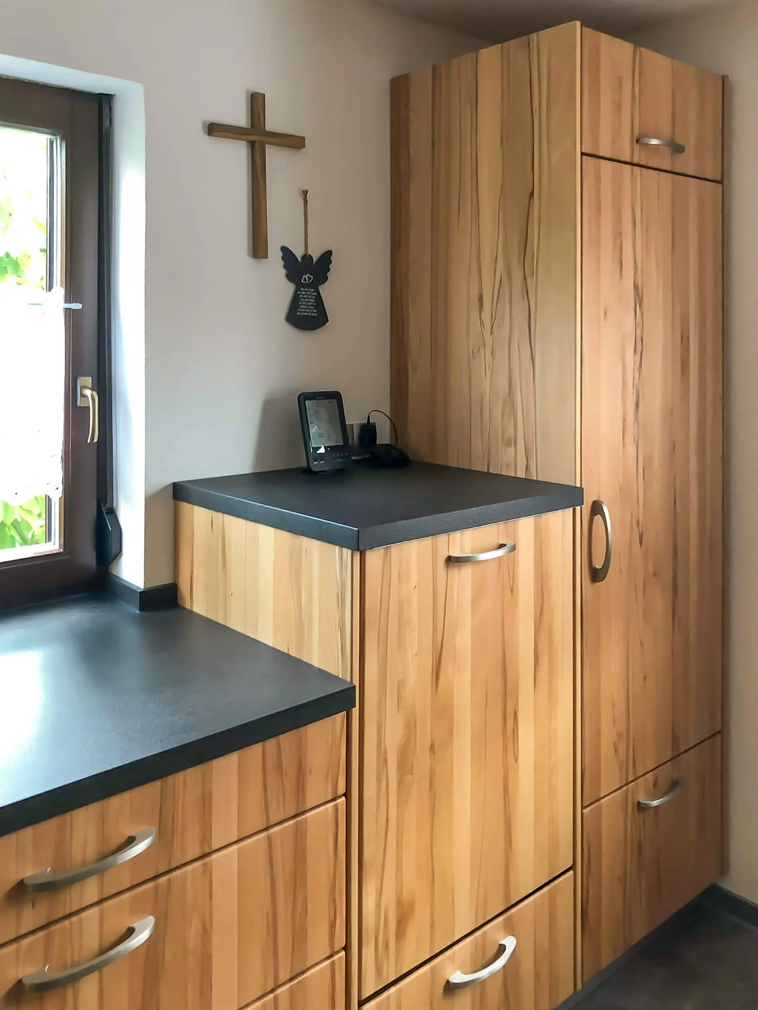 Hochschrank und Unterschränke in Holzfurnier mit dunkler Arbeitsplatte und Fensternische in Küche