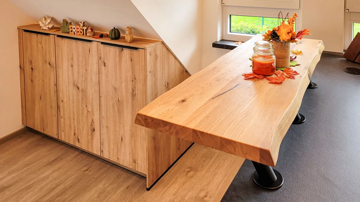 Esstisch mit Baumkante und Trompetenbeinen vor einem Holz-Lowboard im Wohnesszimmer.