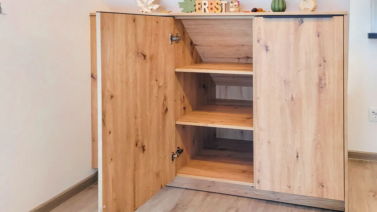 Geöffneter Holz-Beistellschrank mit leeren Einlegeböden und herbstlicher Dekoration.