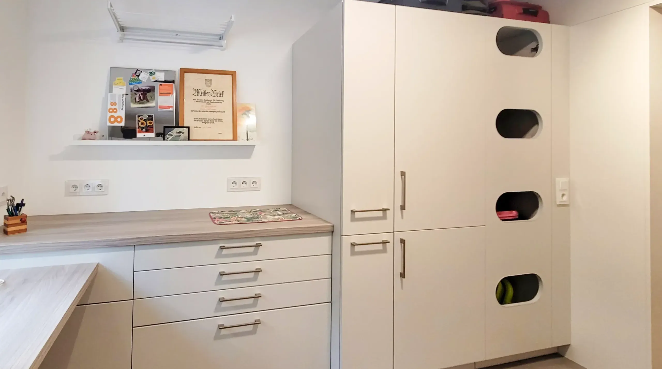 Hauswirtschaftsraum mit integriertem Arbeitsplatz und weißer Schrankwand mit runden Sichtfenstern.