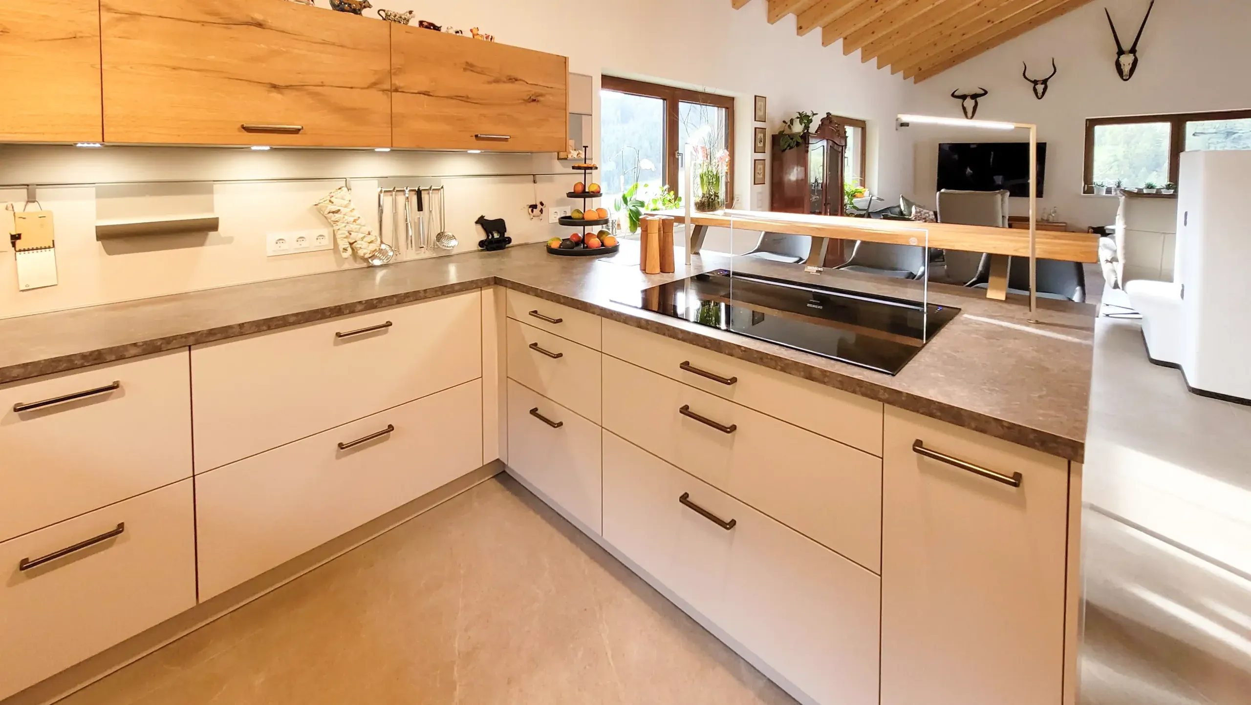 Weiße griffloses U-Küche mit Massivholz-Hochschrankzeile und Holz-Esstheke unter offenem Dachstuhl.