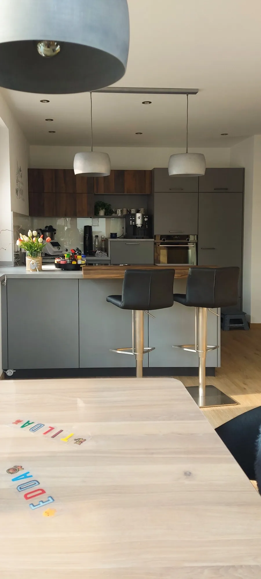 Blick aus dem Wohnbereich auf die graue Halbinsel-Küche mit Holz-Esstheke und Hochschränken