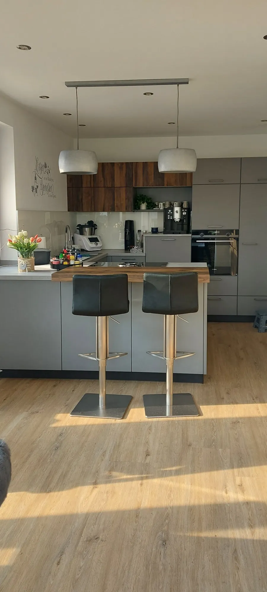 Graue Wohnküche mit Holz-Esstheke, Barhockern, Pendelleuchten und Holz-Hochschränken